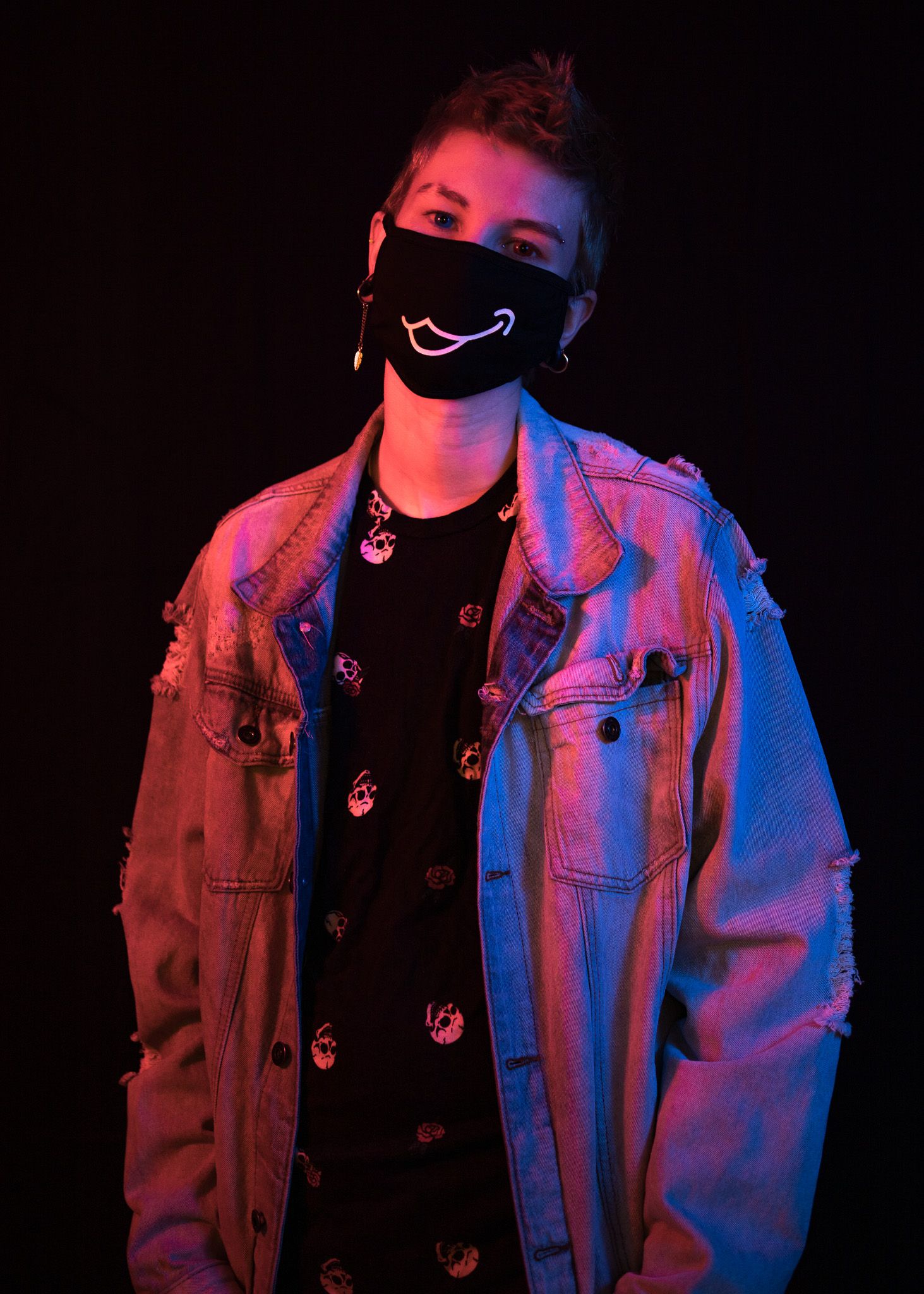 Moody portrait with red and blue lighting wearing denim jacket and face mask.