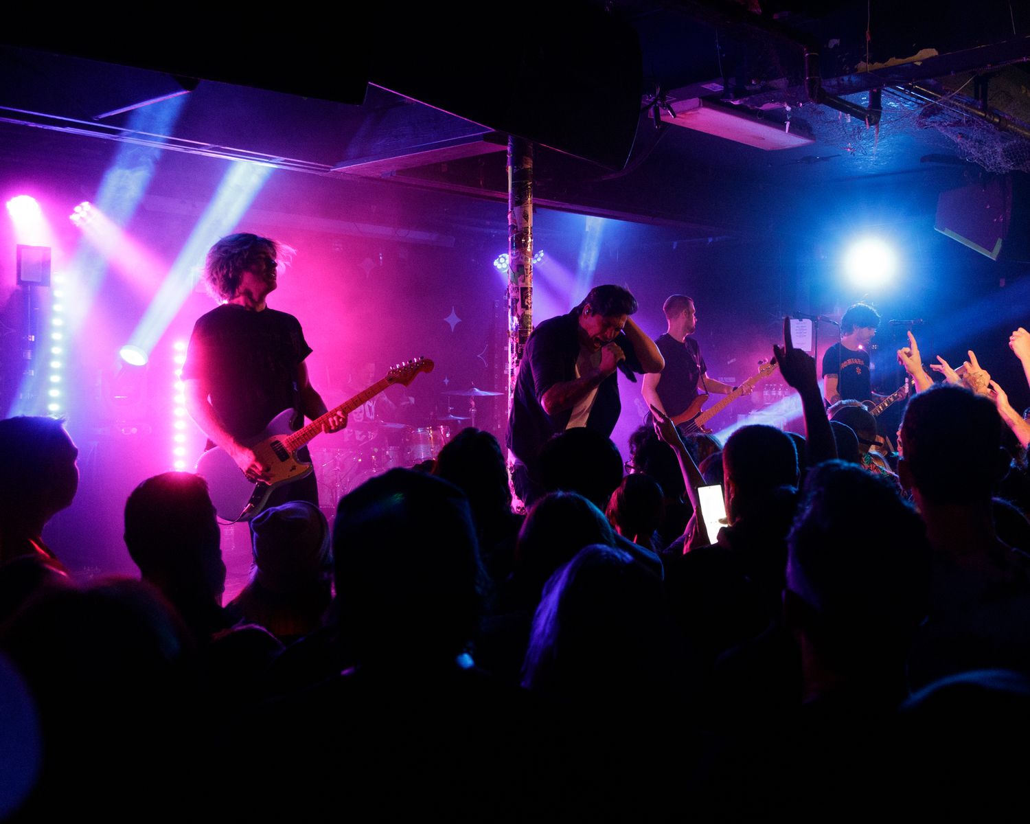Concert venue illuminated with vibrant purple and blue lights as crowd watches performers on stage.
