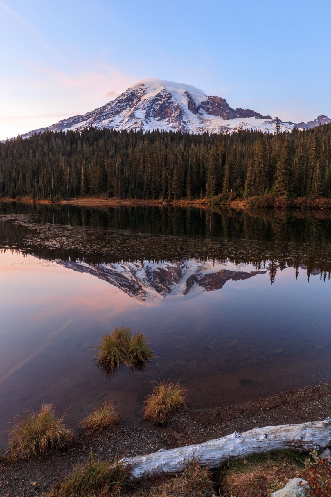 Snow-capped mountain reflects perfectly in calm alpine lake at twilight.