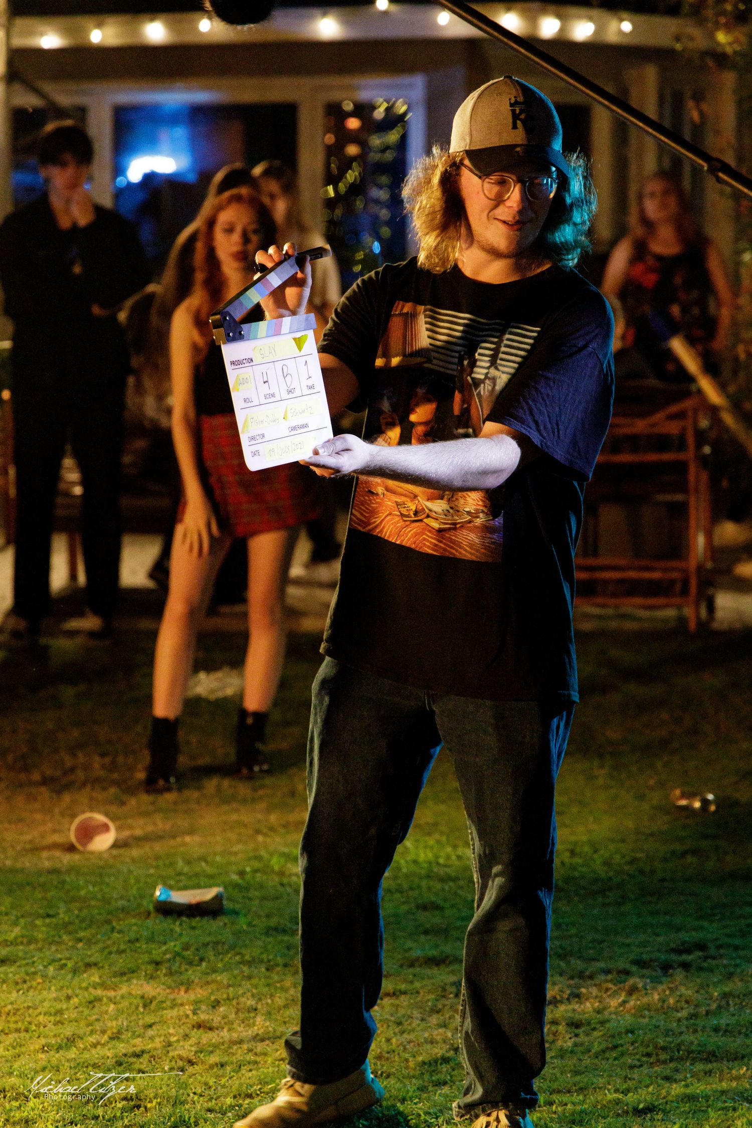 Film crew with clapperboard working on outdoor set with string lights in background.