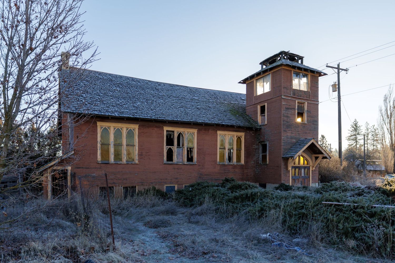 Exterior view of abandoned brick building with tower features in winter landscape setting.