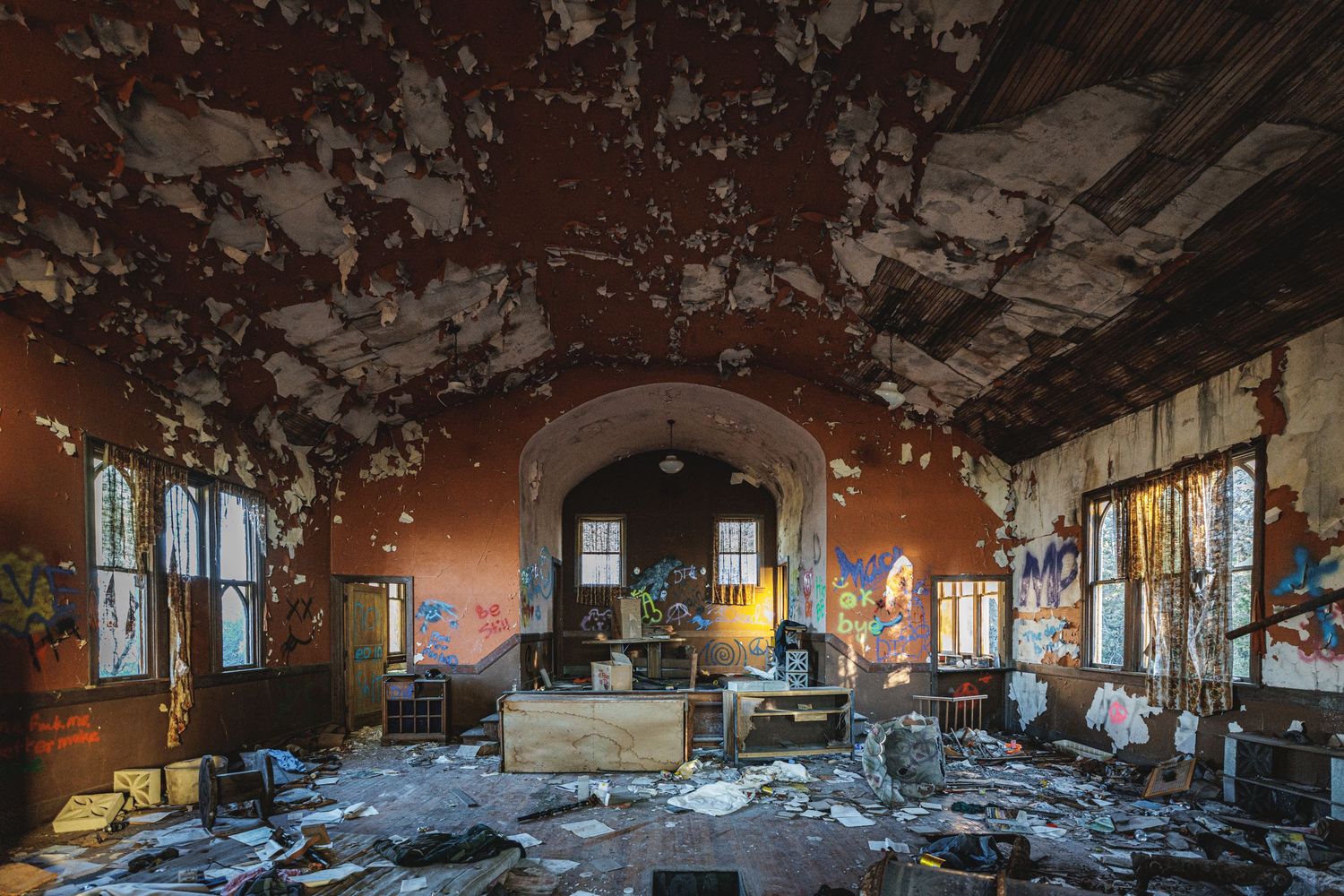 Decaying interior hall of historic building with peeling paint and debris scattered across wooden floor.