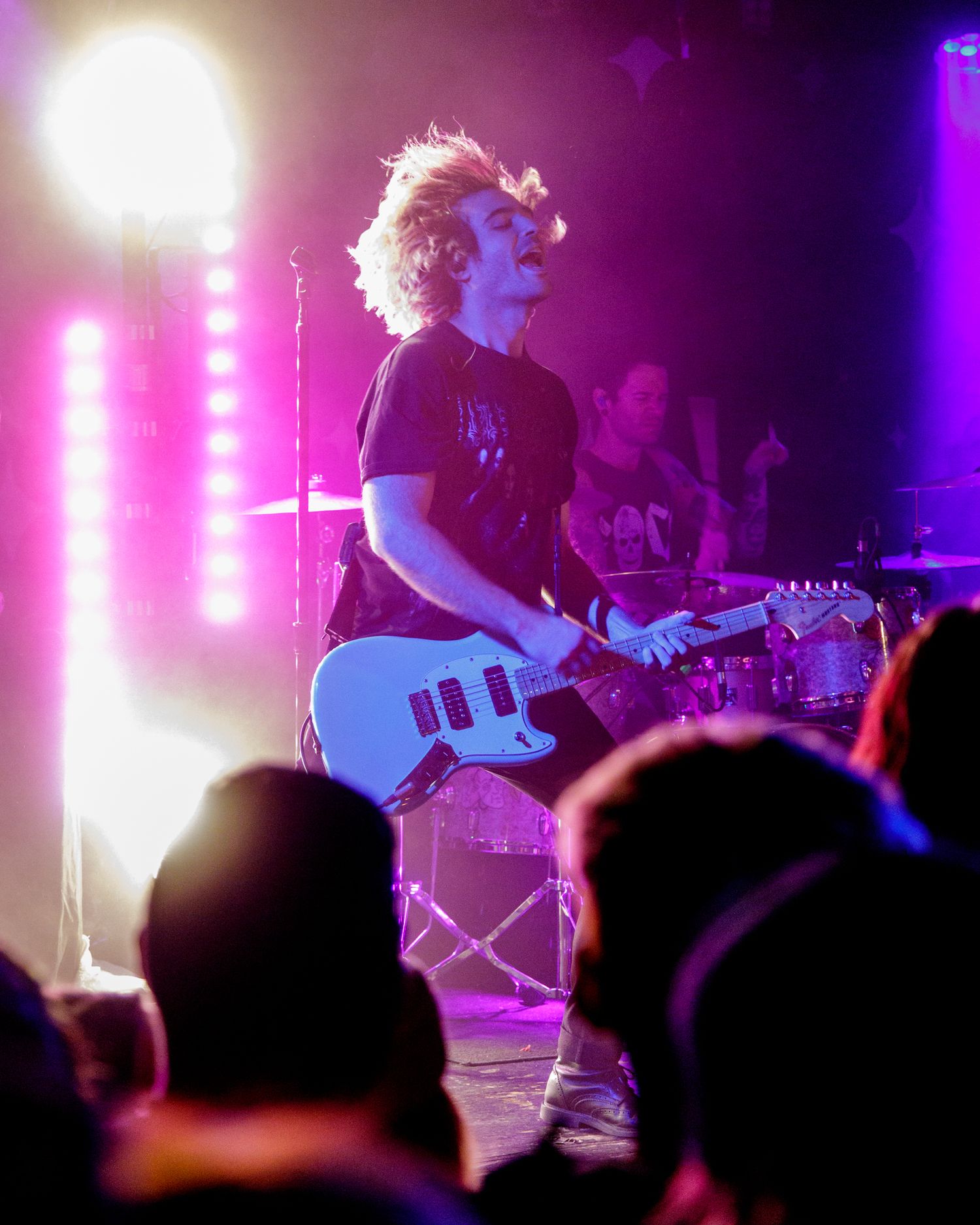 Rock band performs on stage with purple lighting and silhouetted crowd.