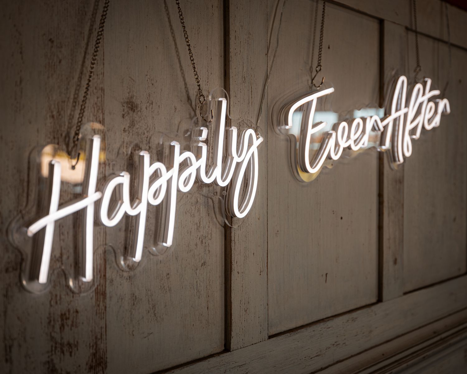 Neon sign reading 'Happily Ever After' mounted on a textured wall in cursive lettering.