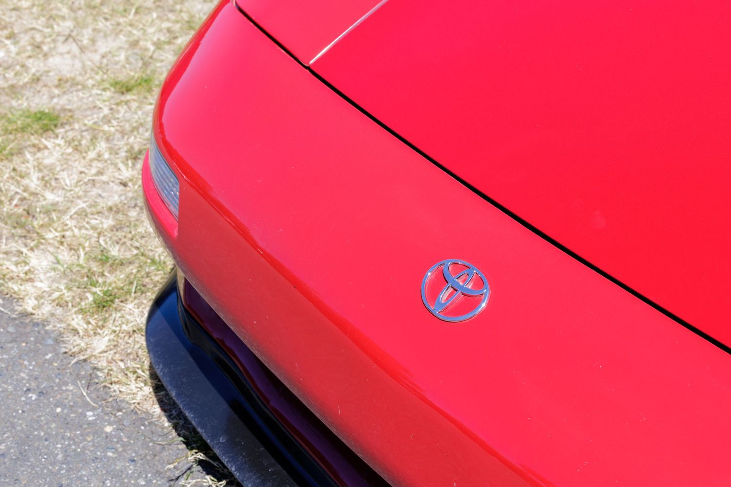 Close-up of a red Toyota car hood featuring the iconic blue Toyota emblem badge on a sunny day.