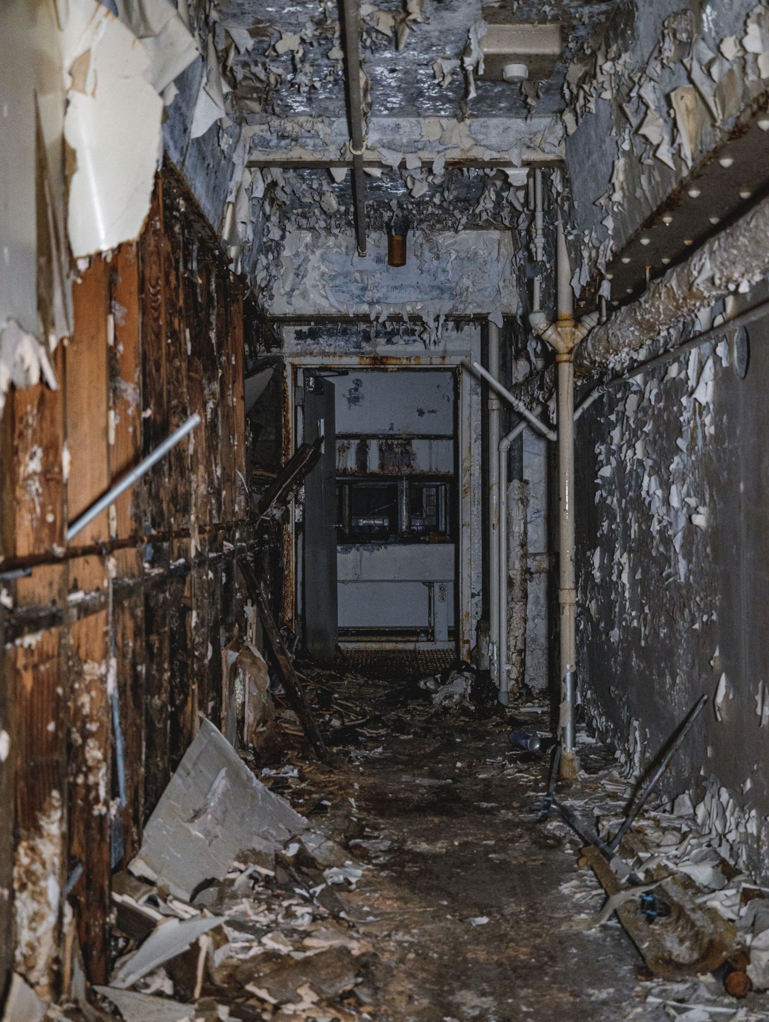 Deteriorating hallway with peeling walls and exposed infrastructure.