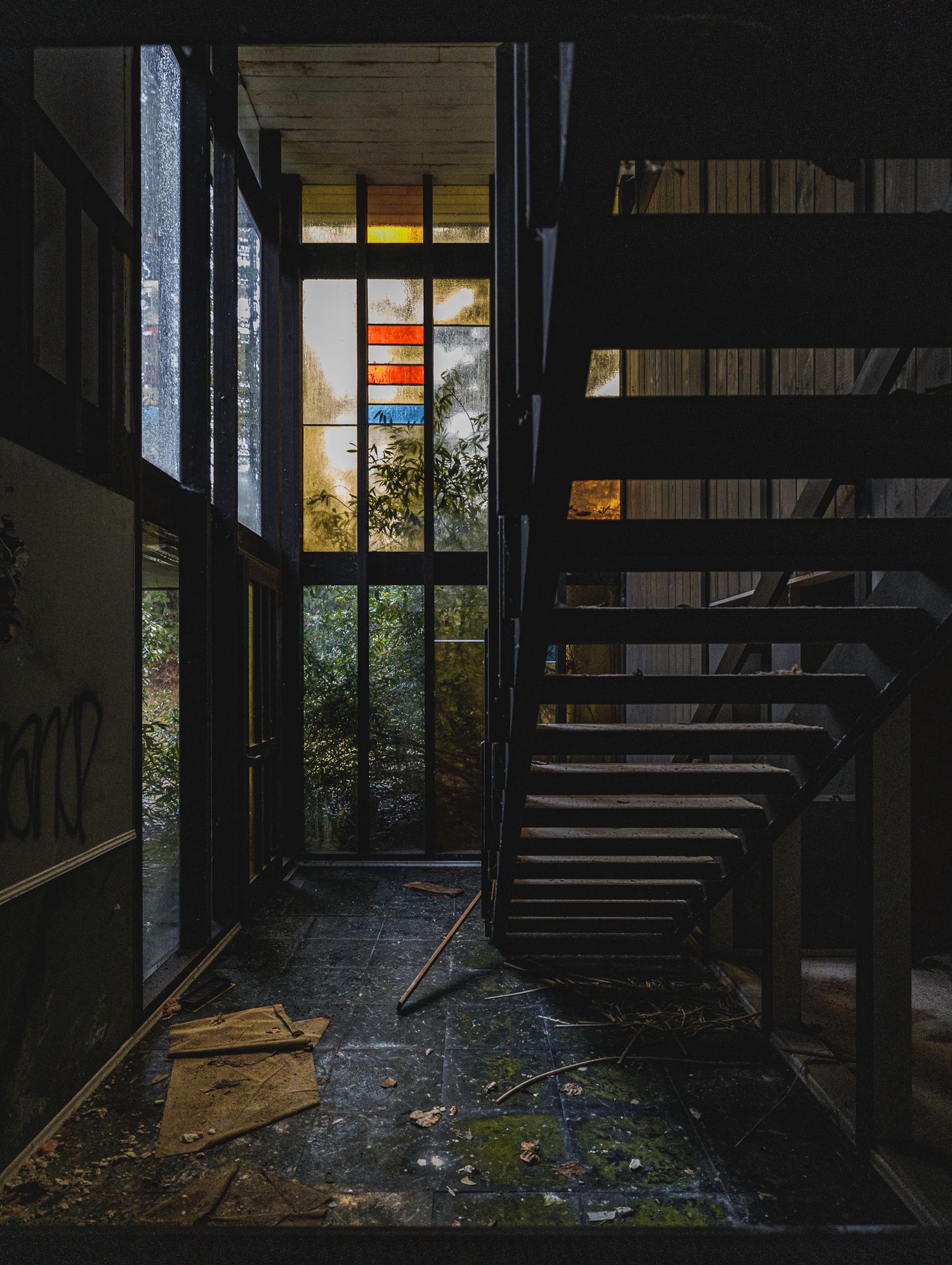 Abandoned interior stairwell with broken debris and sunlight filtering through windows.