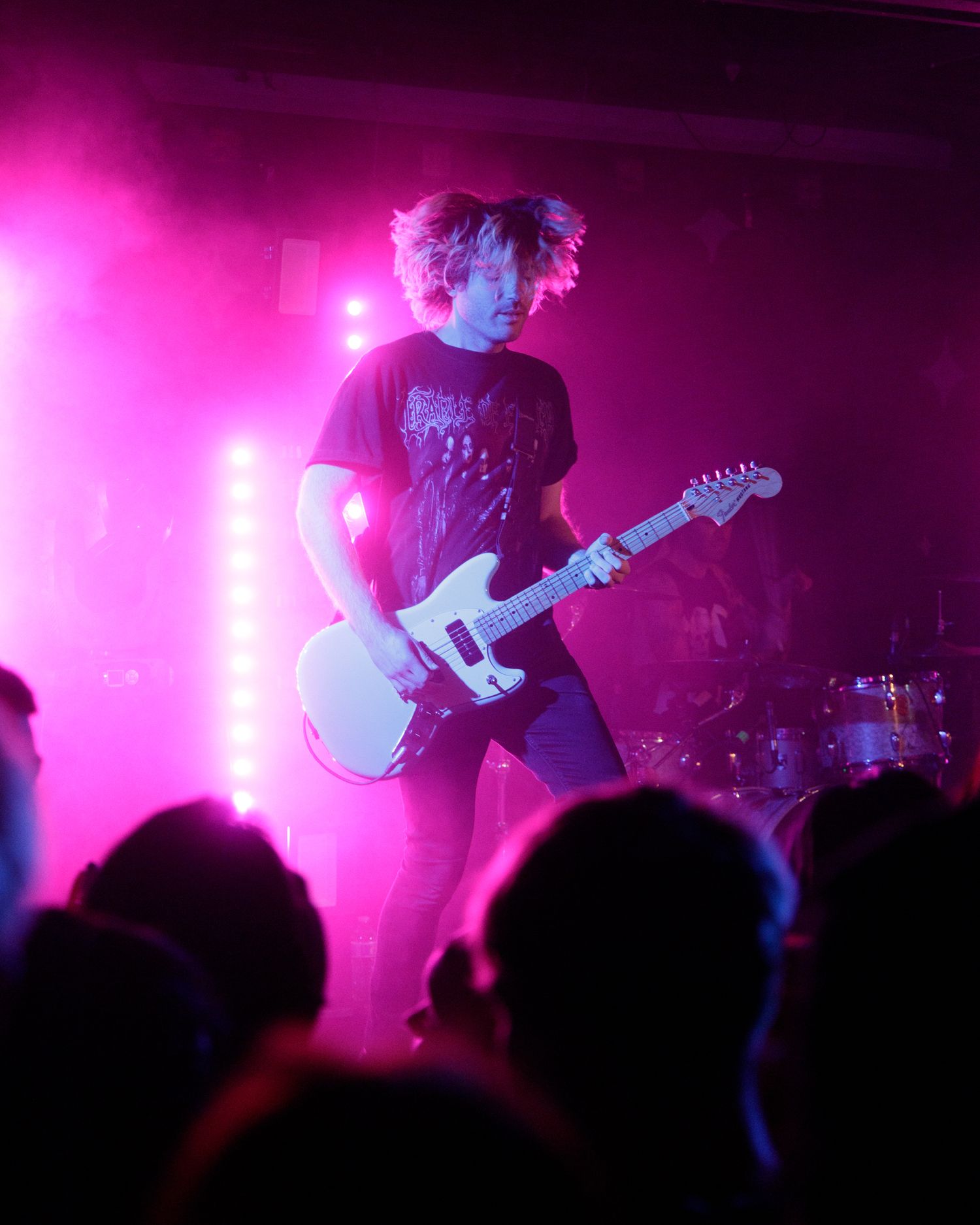 Musicians playing guitars bathed in bright pink stage lighting during live performance.