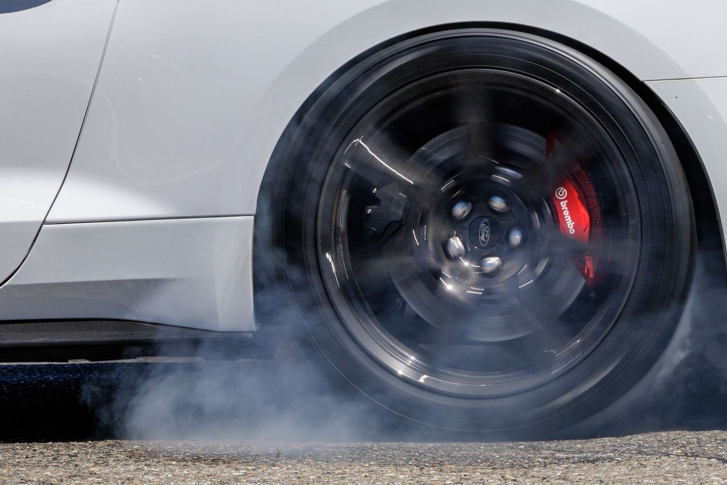 Close-up of a spinning black alloy wheel with red brake calipers emitting smoke during a car burnout.