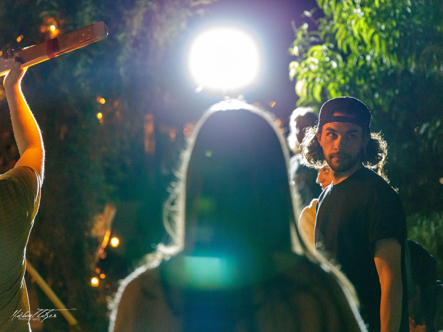 Film crew working on an outdoor nighttime shoot with bright lighting equipment.