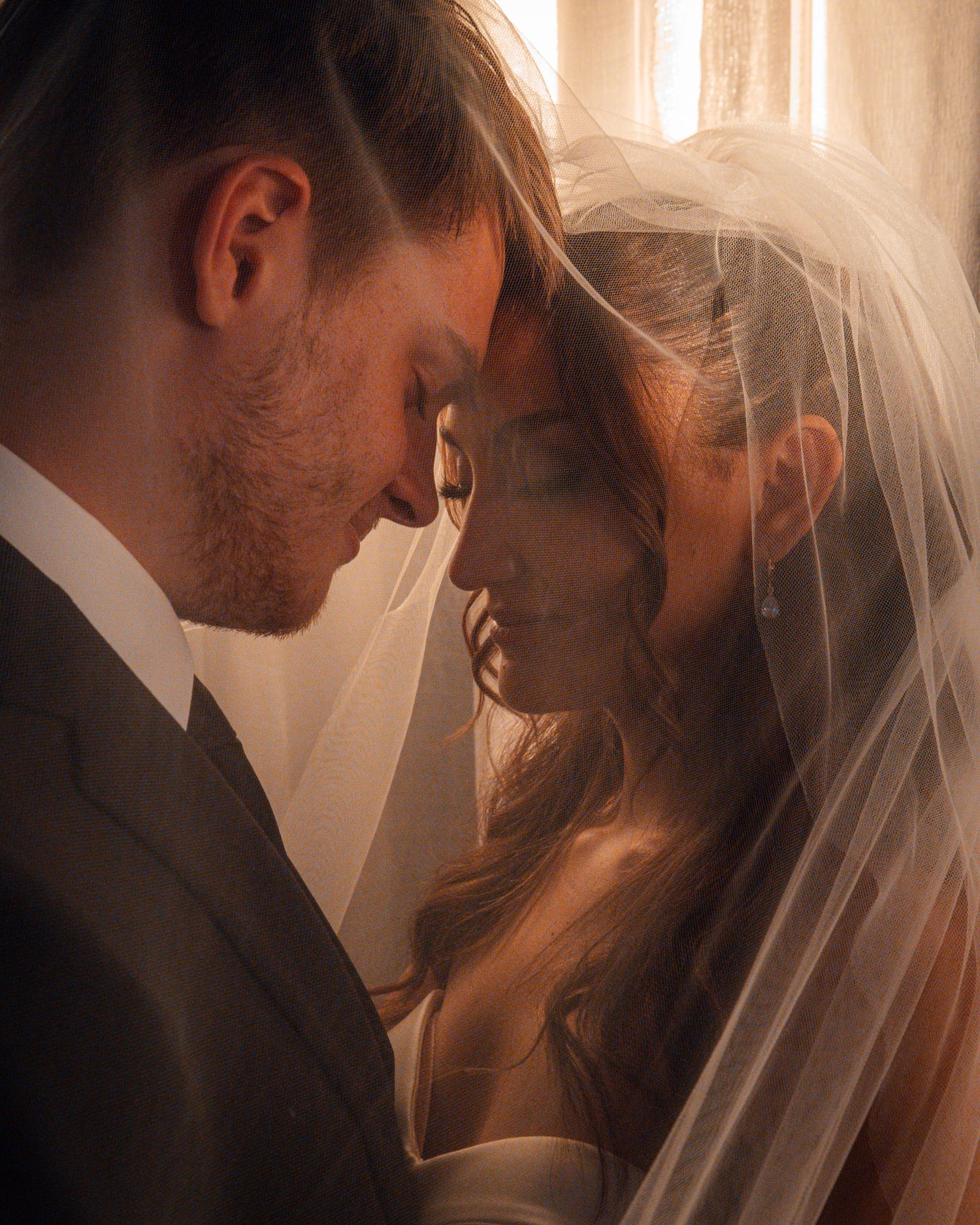 Intimate wedding couple portrait with soft lighting and flowing veil creating romantic atmosphere.