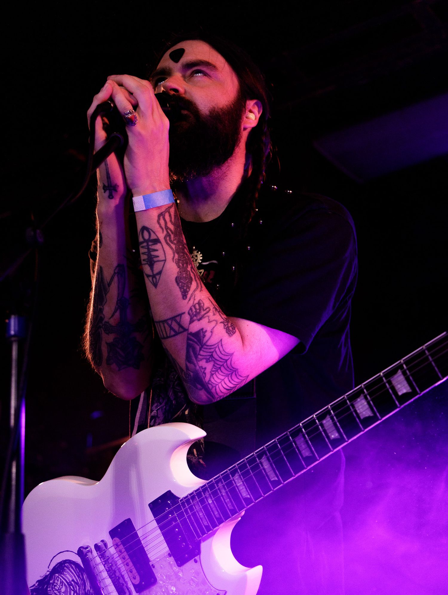 Close-up of musician performing with guitar under purple stage lighting.
