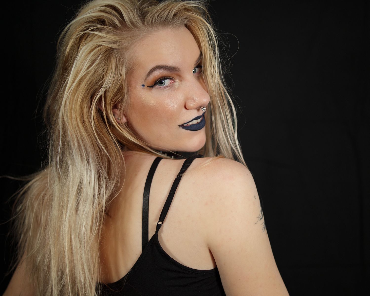 Studio portrait with dramatic lighting featuring blue lipstick and blonde hair against dark background.