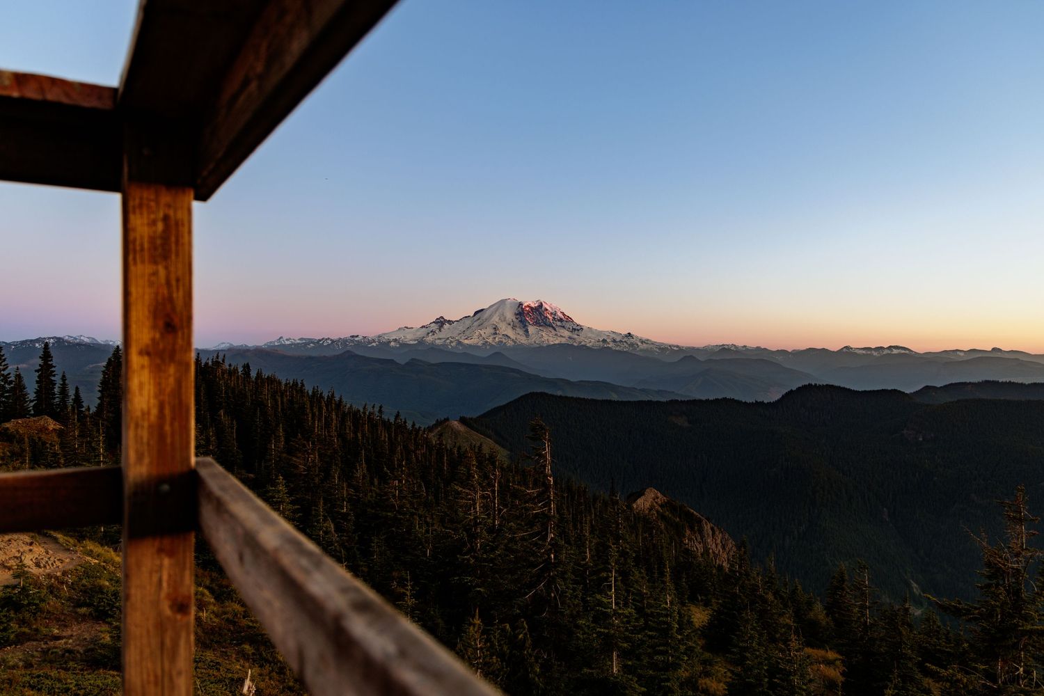 Mountain vista seen through wooden pillars at sunset with distant peaks silhouetted against the sky.