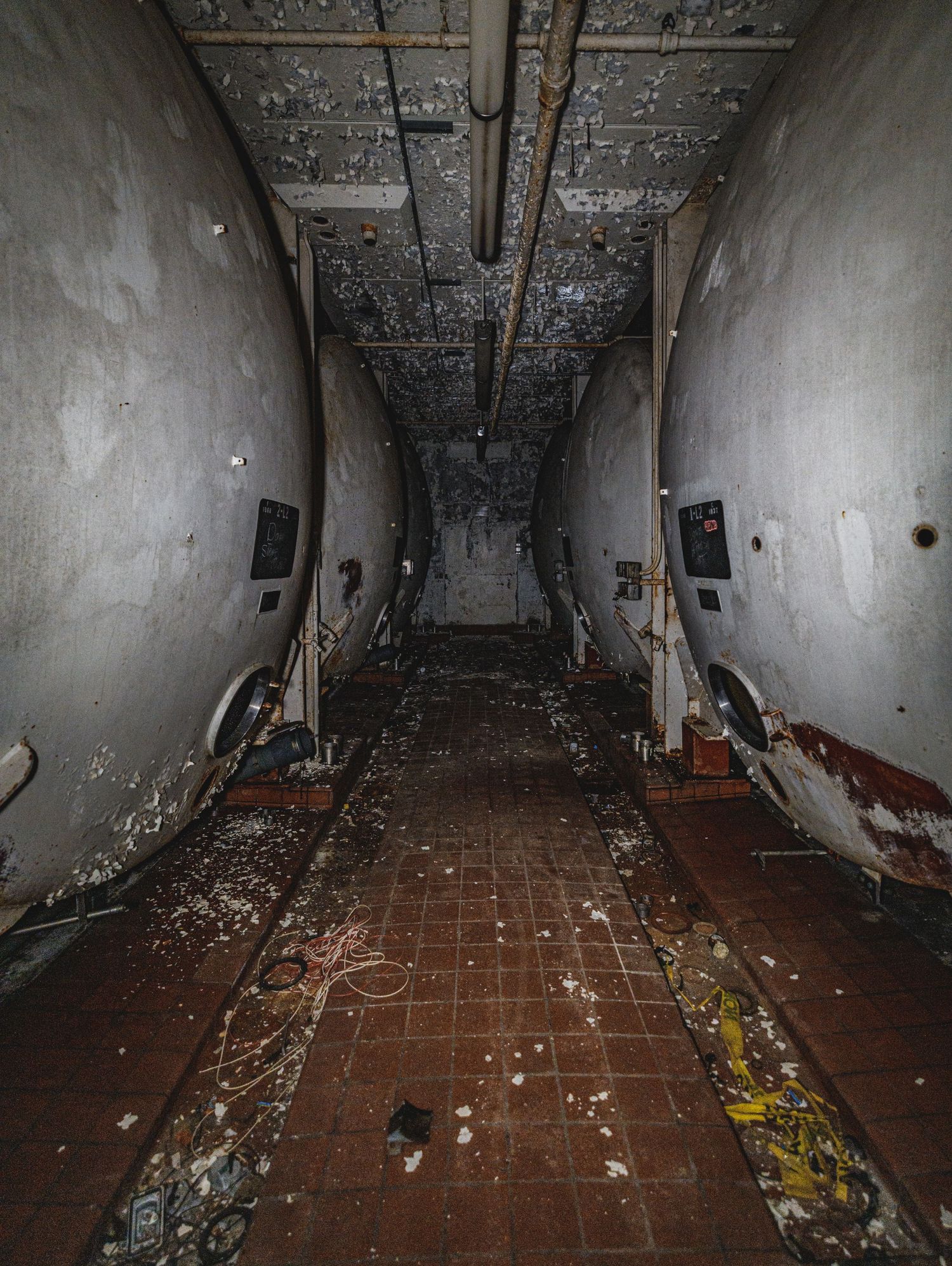 Narrow corridor with red tile floor and curved walls in an abandoned basement.