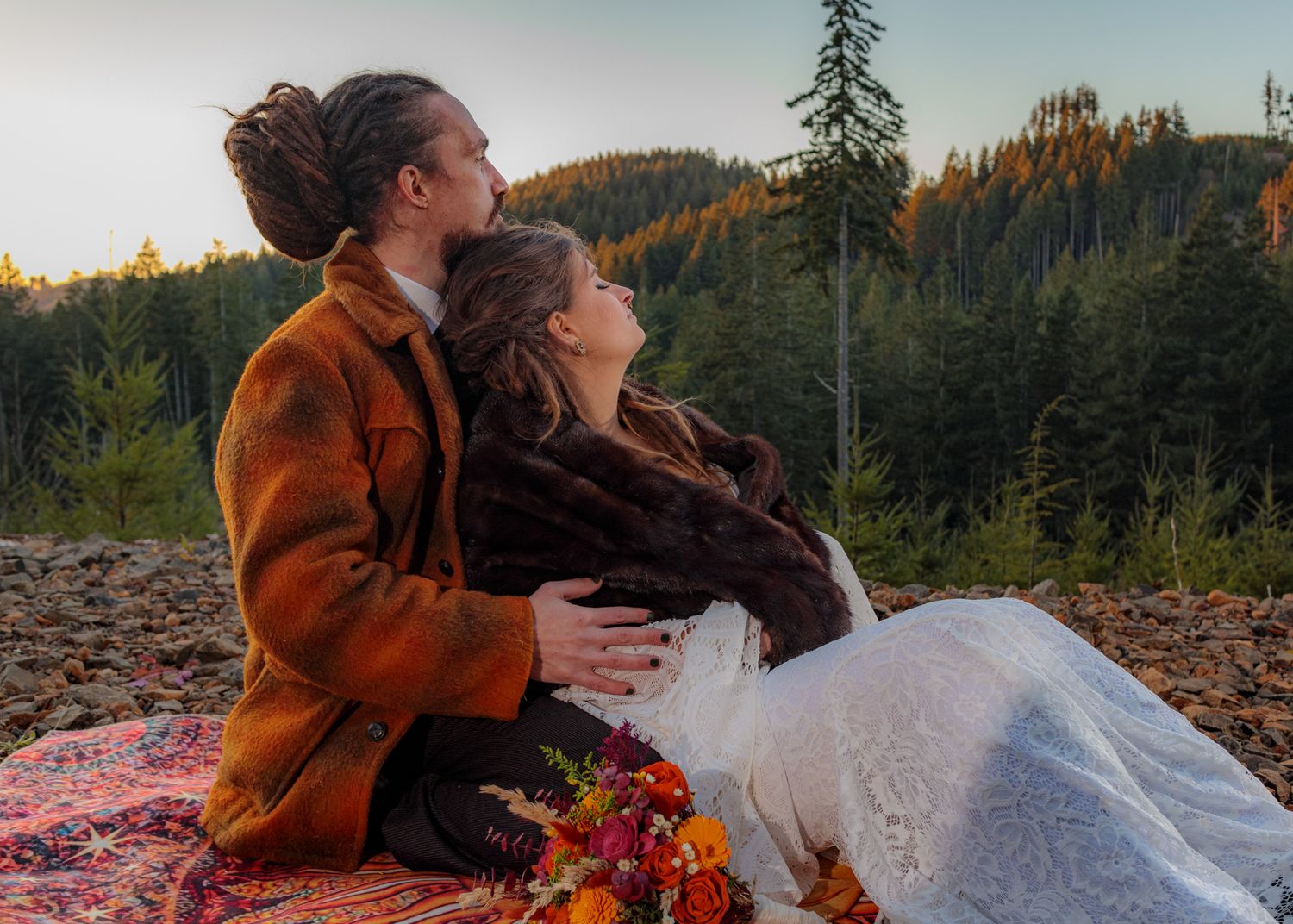 A romantic photoshoot on rocky terrain with mountains and forest in the background.