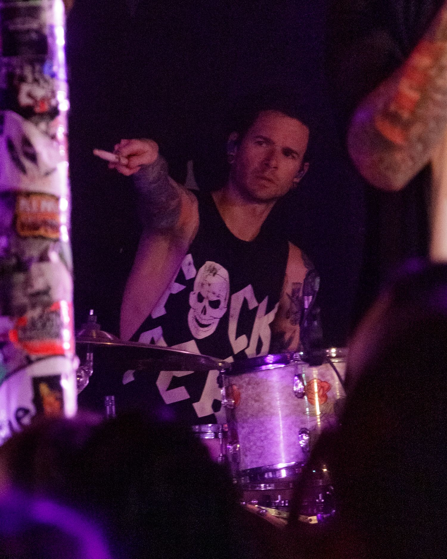 Drummer performing on stage with purple lighting and concert venue decorations visible.