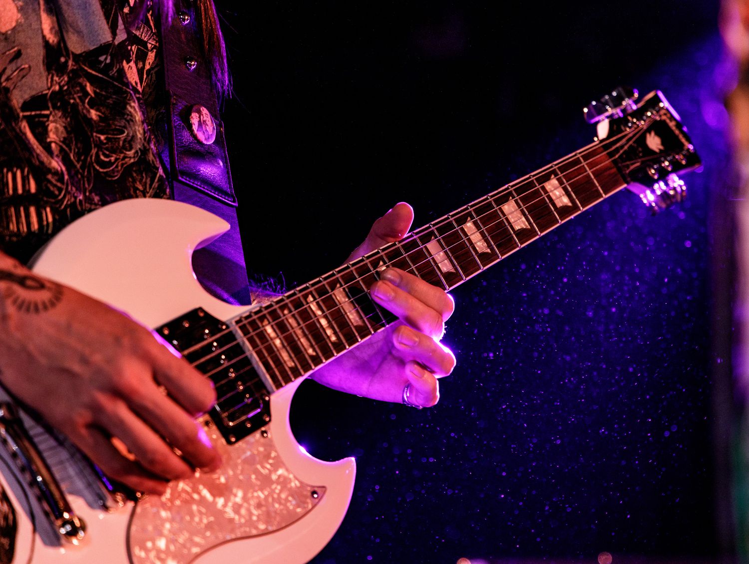 Close-up shot of hands playing an electric guitar with pink stage lighting.