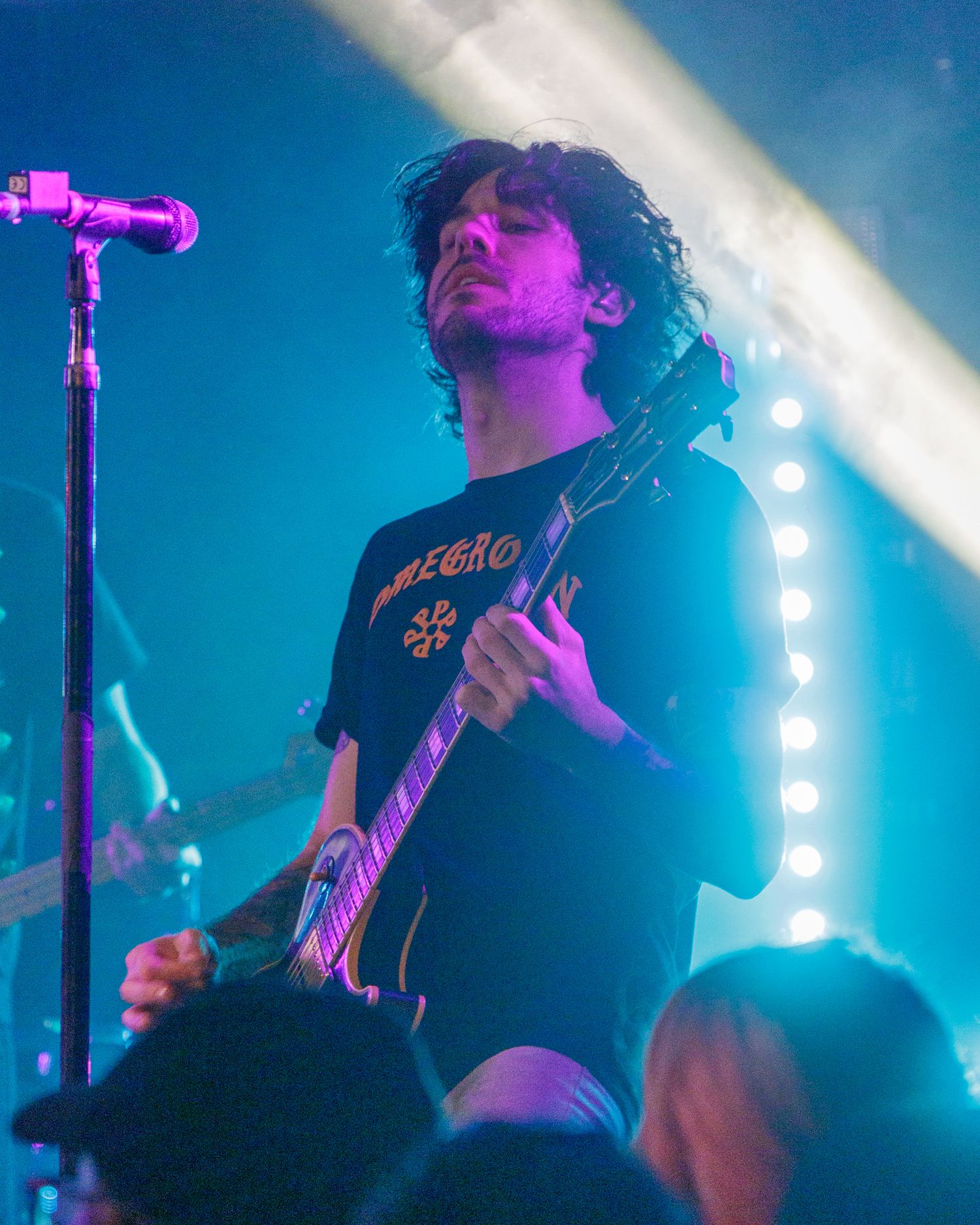 Guitarist on stage illuminated by dramatic blue spotlights during concert performance.