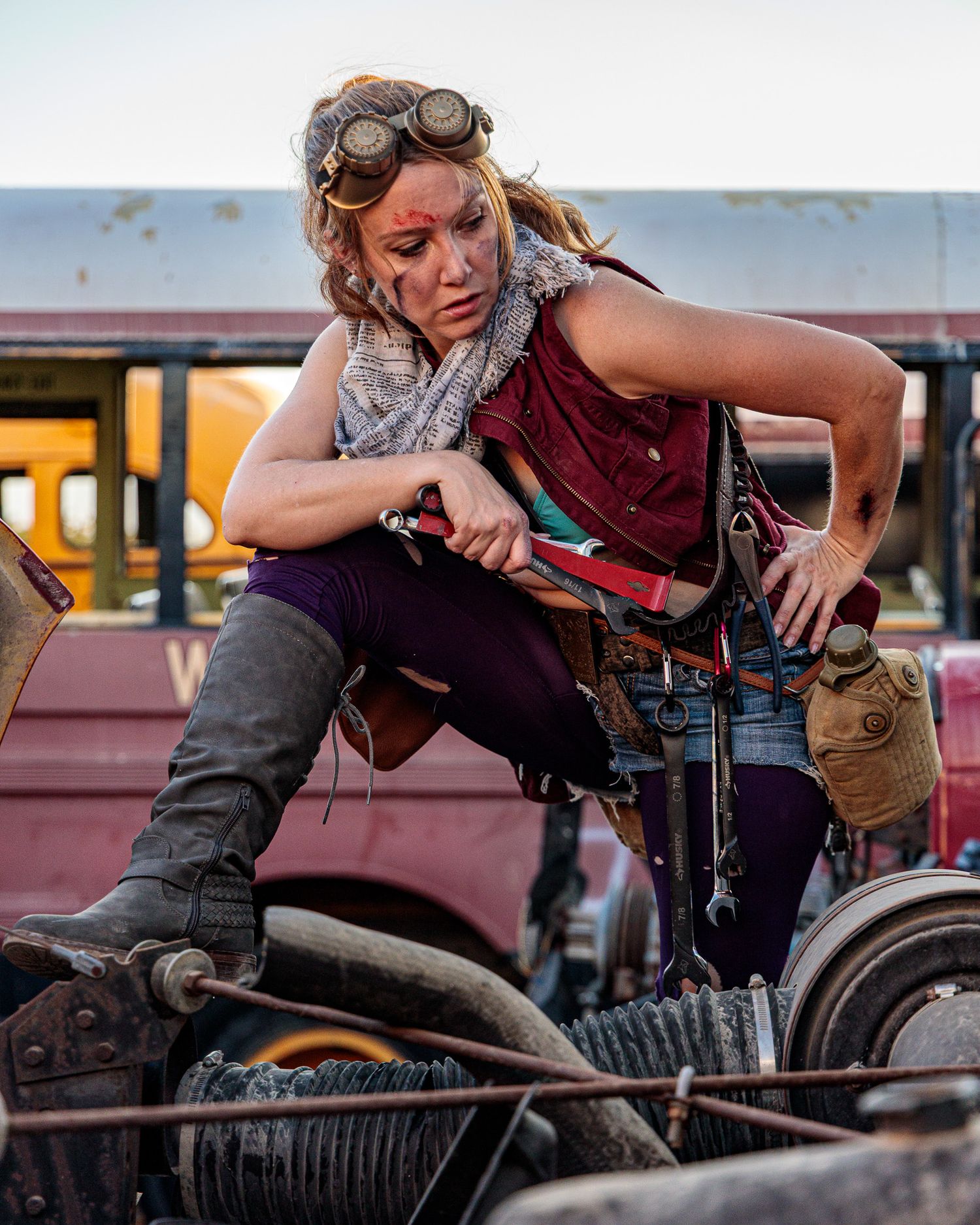 A mechanic in steampunk-style goggles works on an engine in a post-apocalyptic setting.