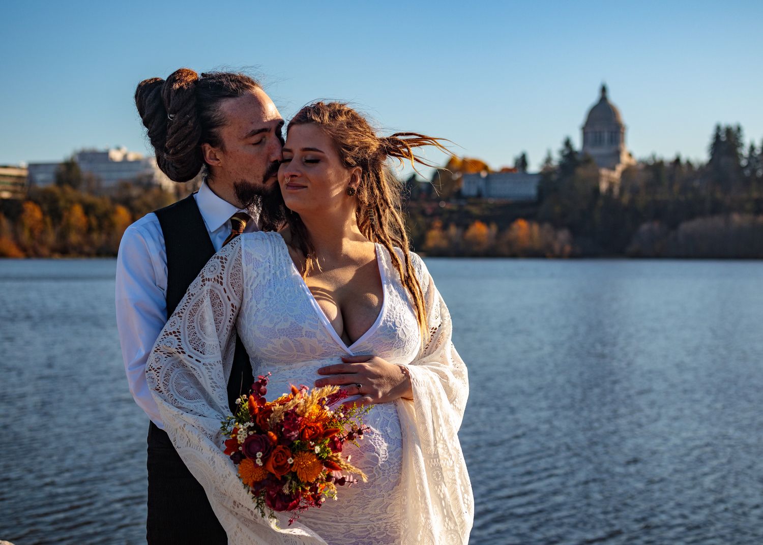 Lakeside wedding portraits with autumn colors and cityscape in background.