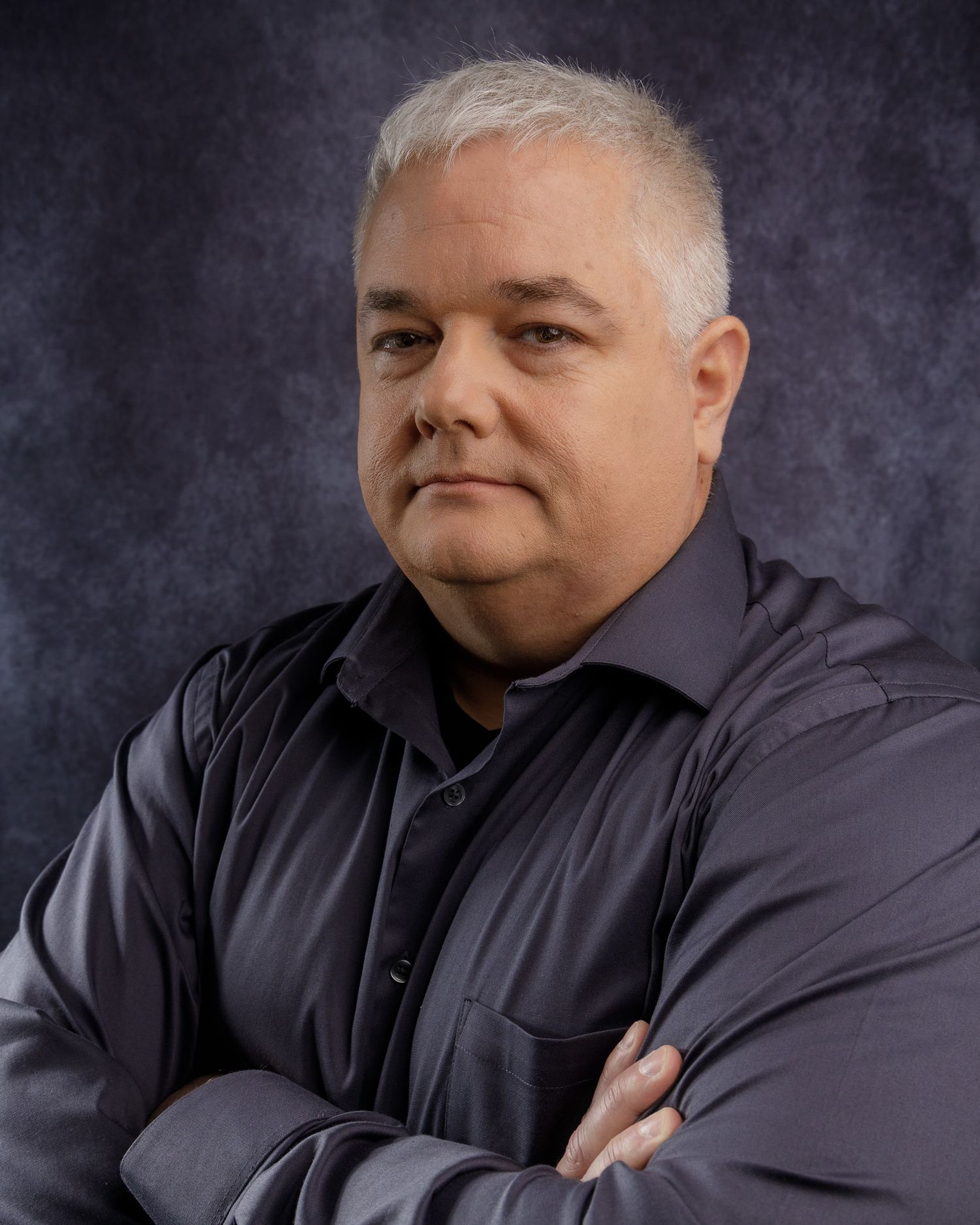 Professional headshot of person in dark clothing against textured grey background.