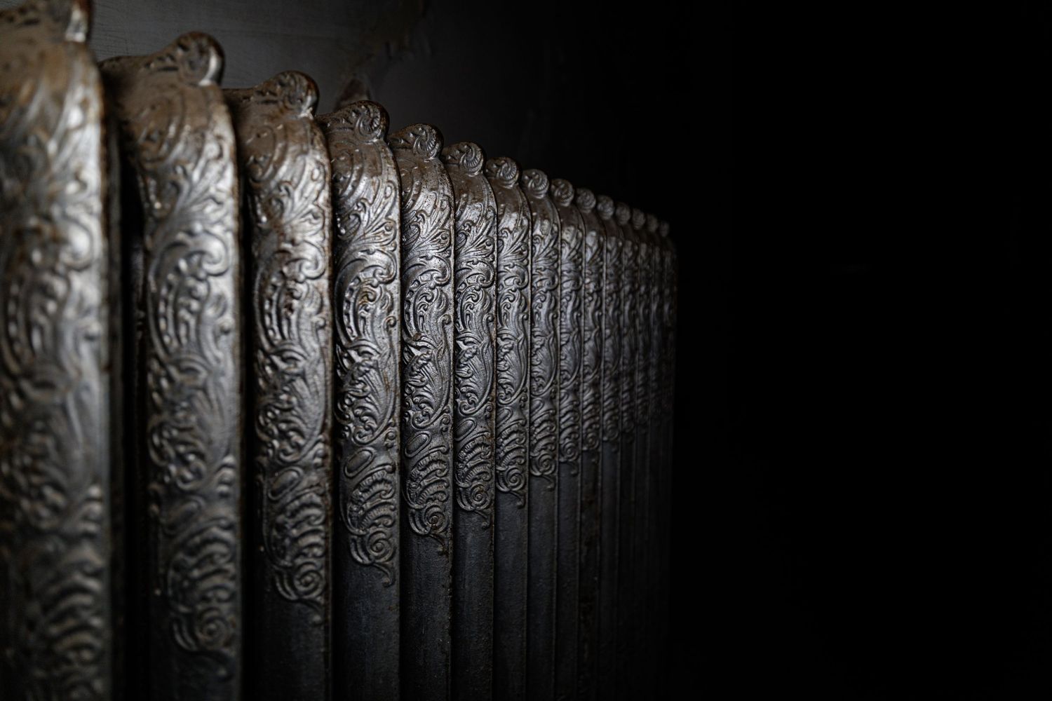 Repeating ornate black metal fence posts create a dramatic vanishing point perspective against a dark background.