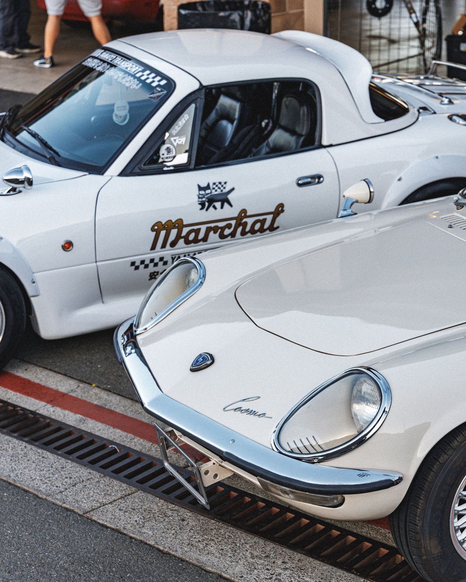 Side profile of a lowered white classic car with Marchal livery parked on street.