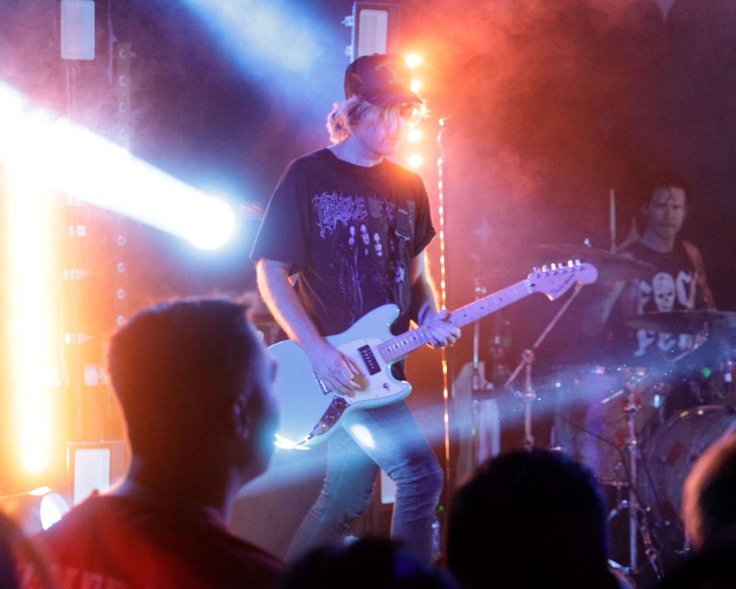 Musicians performing under multicolored stage lights with crowd silhouettes visible below.