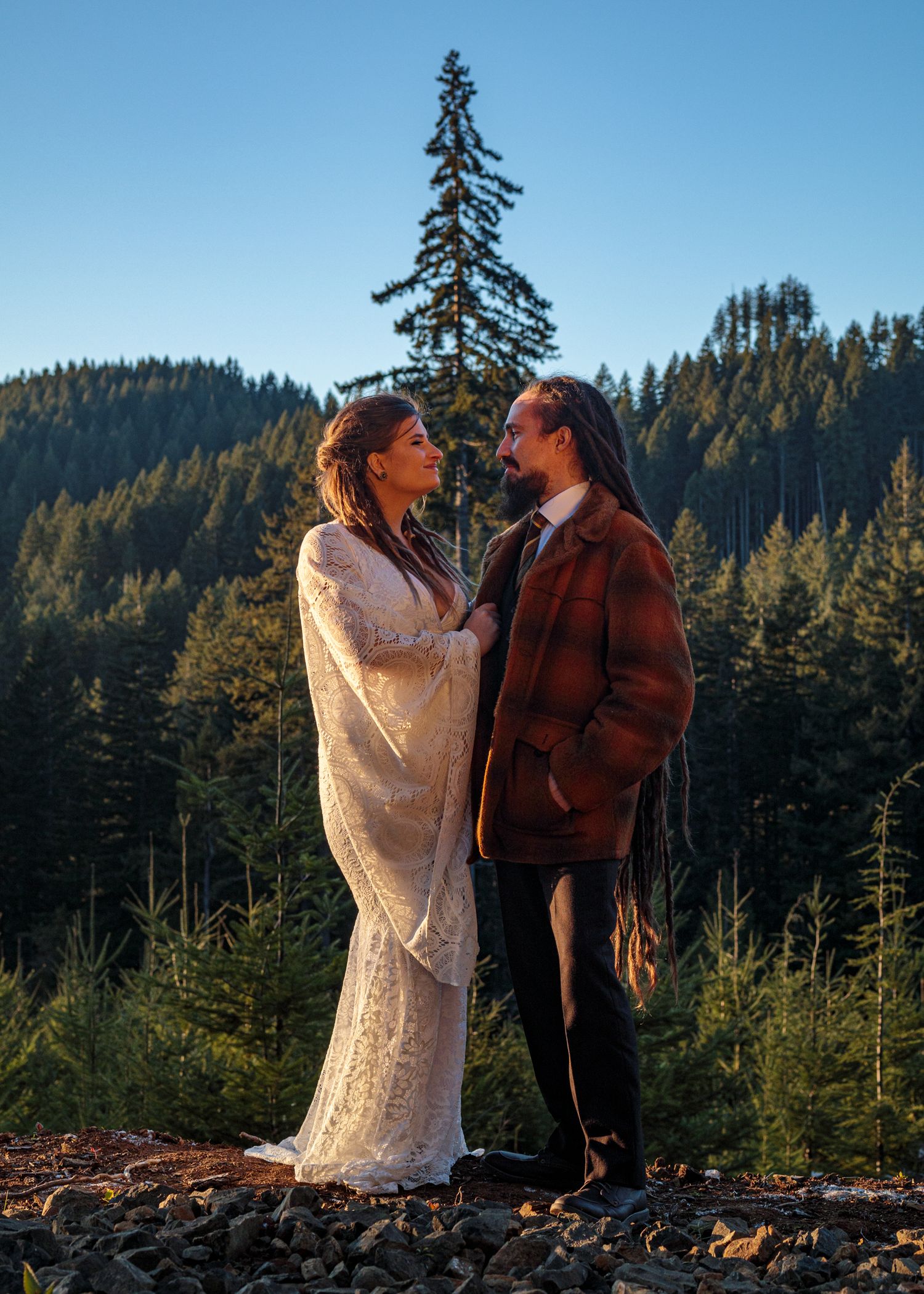 A romantic outdoor photoshoot with a white lace dress against a mountainous forest backdrop.