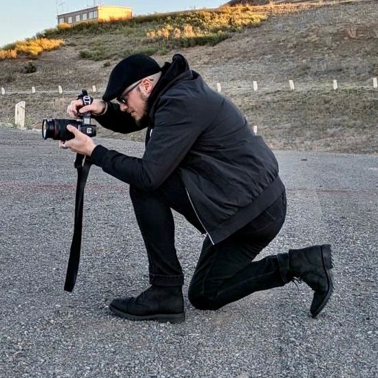 Person in black clothing practices various photography positions on gravel surface.