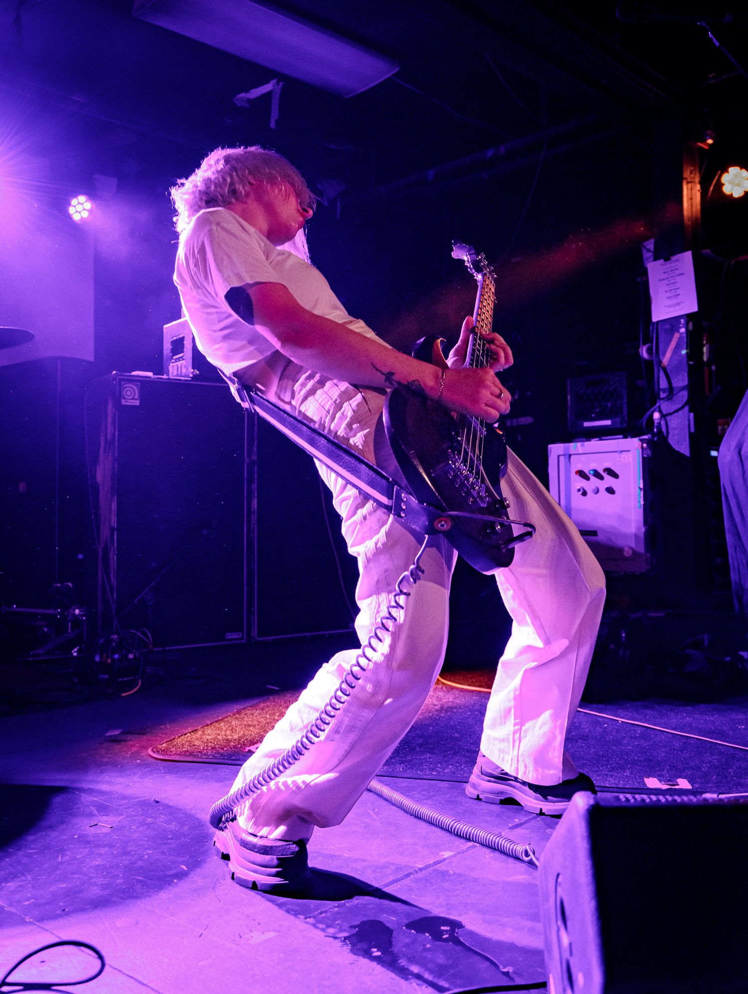 Dynamic shots of performers in white pants playing instruments on a dark stage with purple lighting.