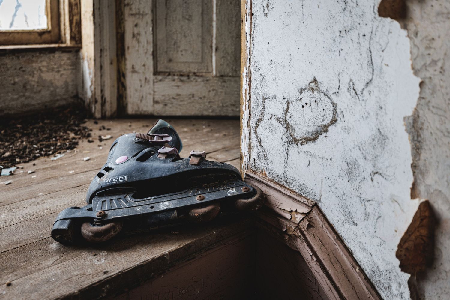 Decaying interior hallway with peeling paint and debris scattered across the floor.