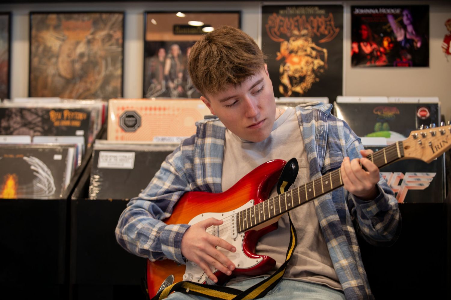 Musician playing electric guitar in record store surrounded by album covers on wall.