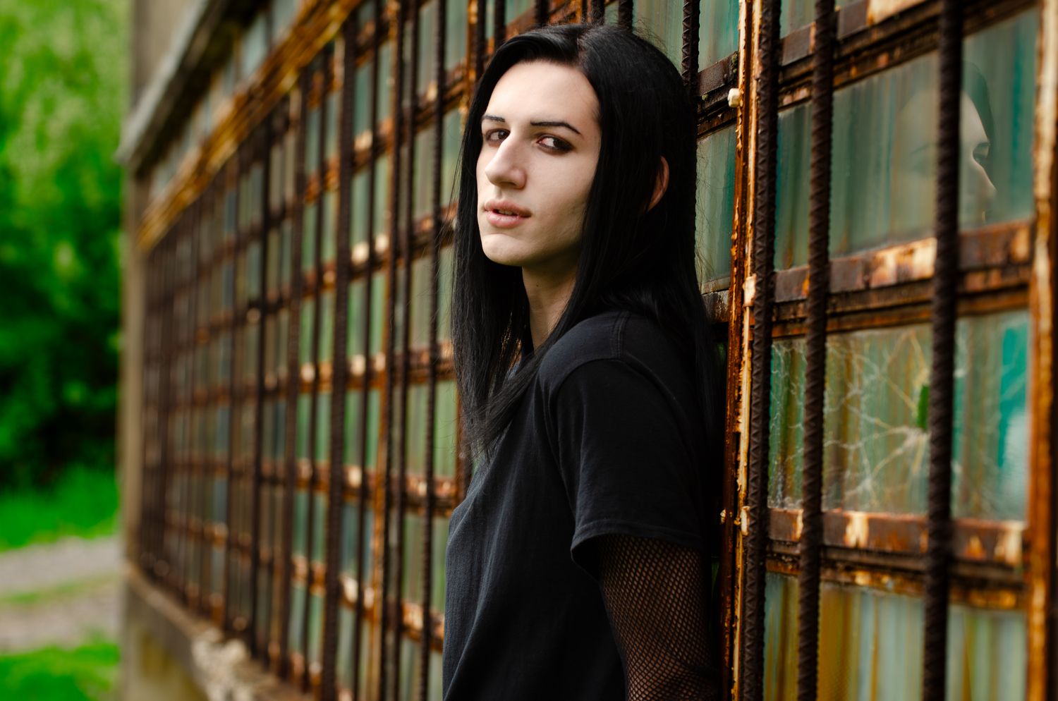 Person in black hoodie leaning against rustic metal window frame.