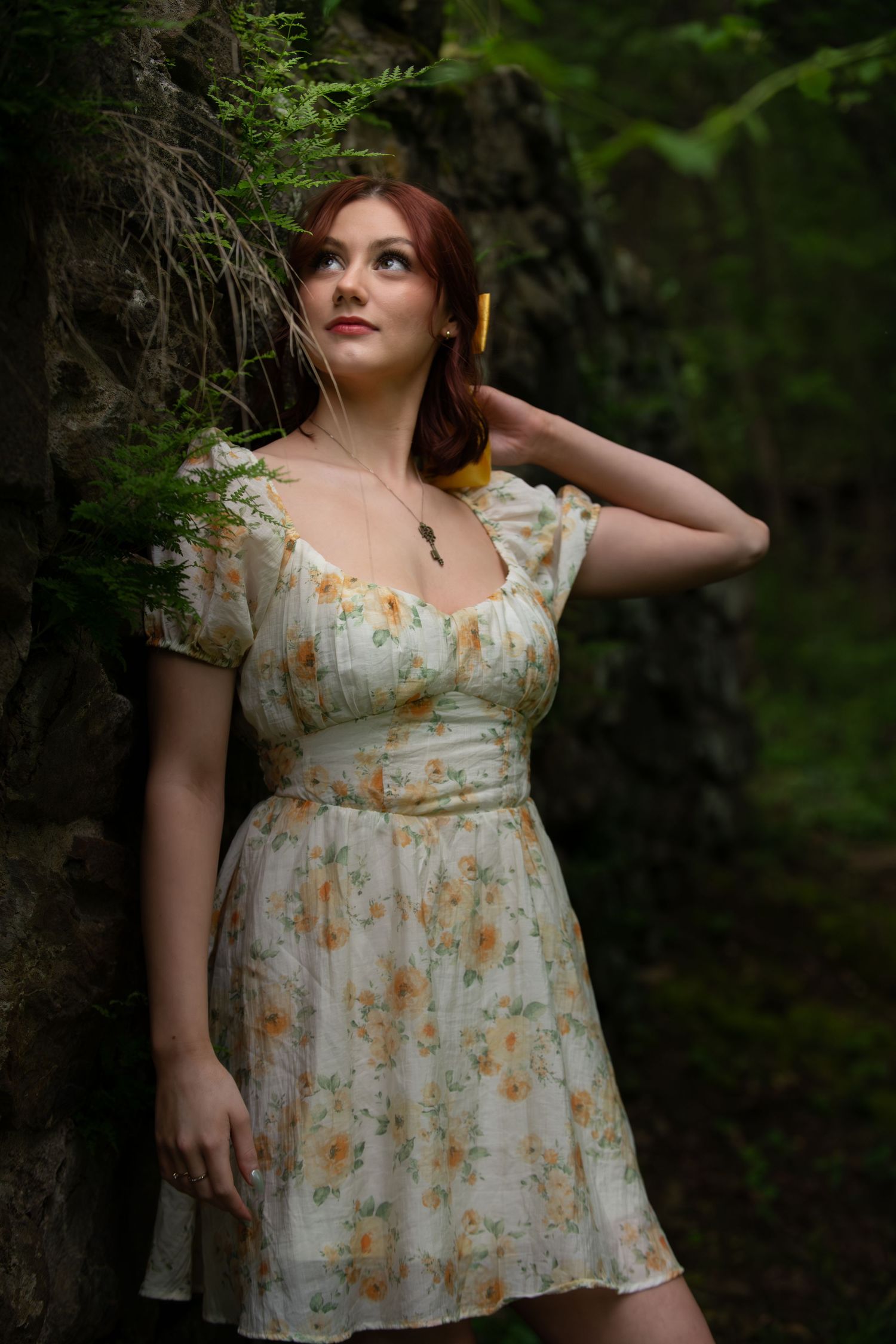 A romantic portrait in a floral summer dress against a mossy stone wall backdrop.