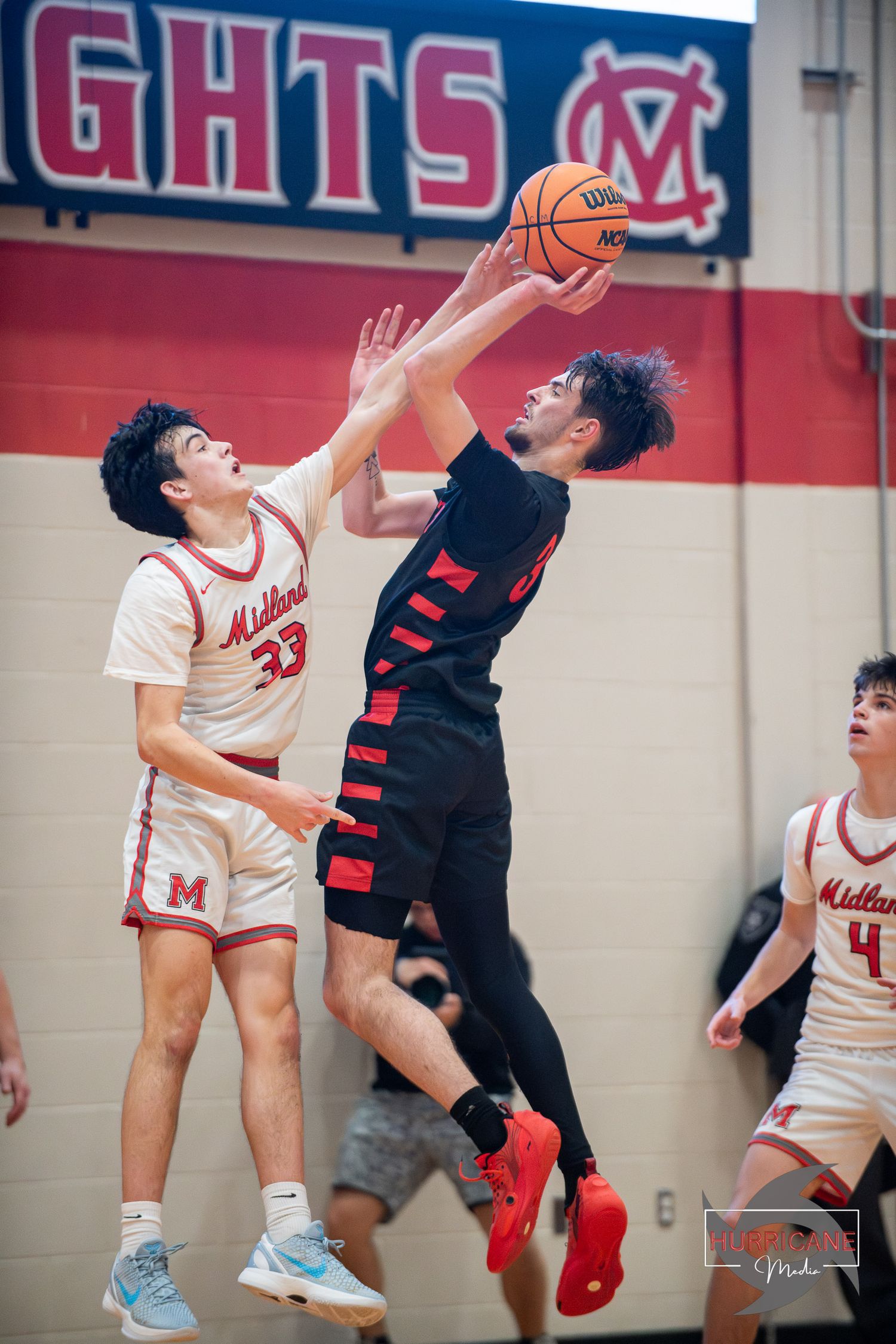 Two basketball players leap high to compete for possession of the ball during an intense game sequence.
