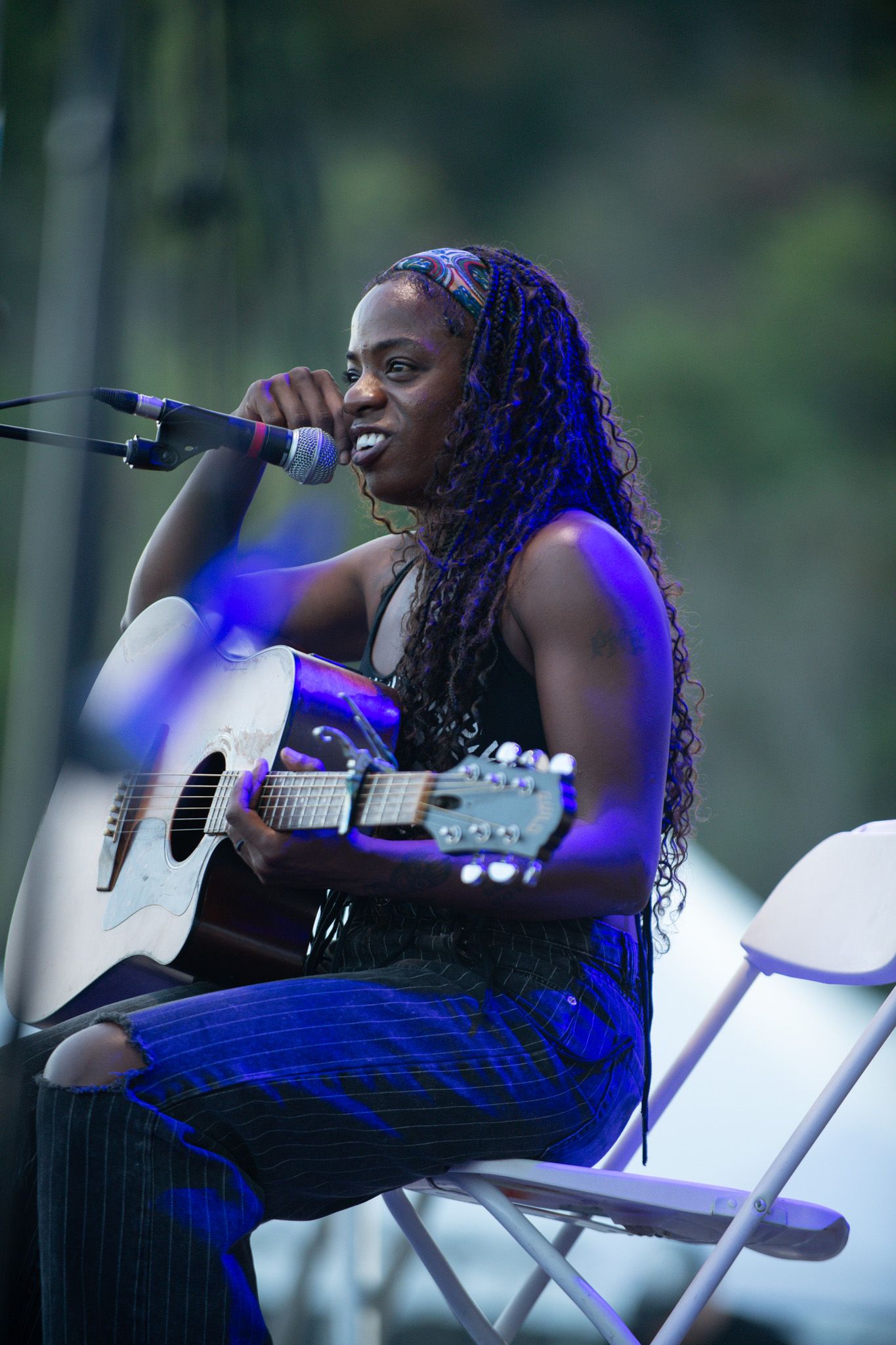 Musician performs passionately with an acoustic guitar on outdoor stage under blue lighting during evening concert.