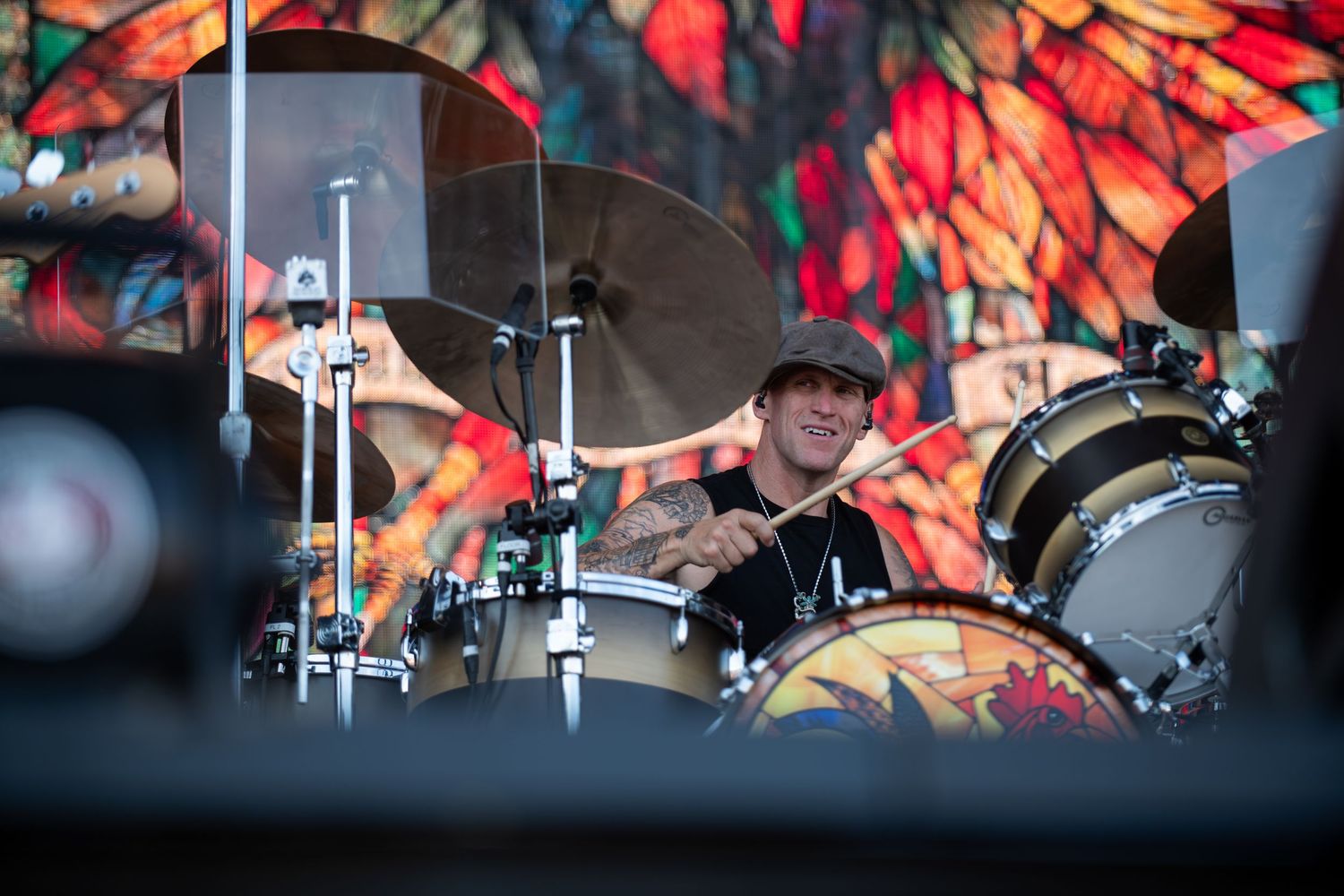 Drummer performs behind a drum kit on stage with vibrant red and colorful backdrop lighting.