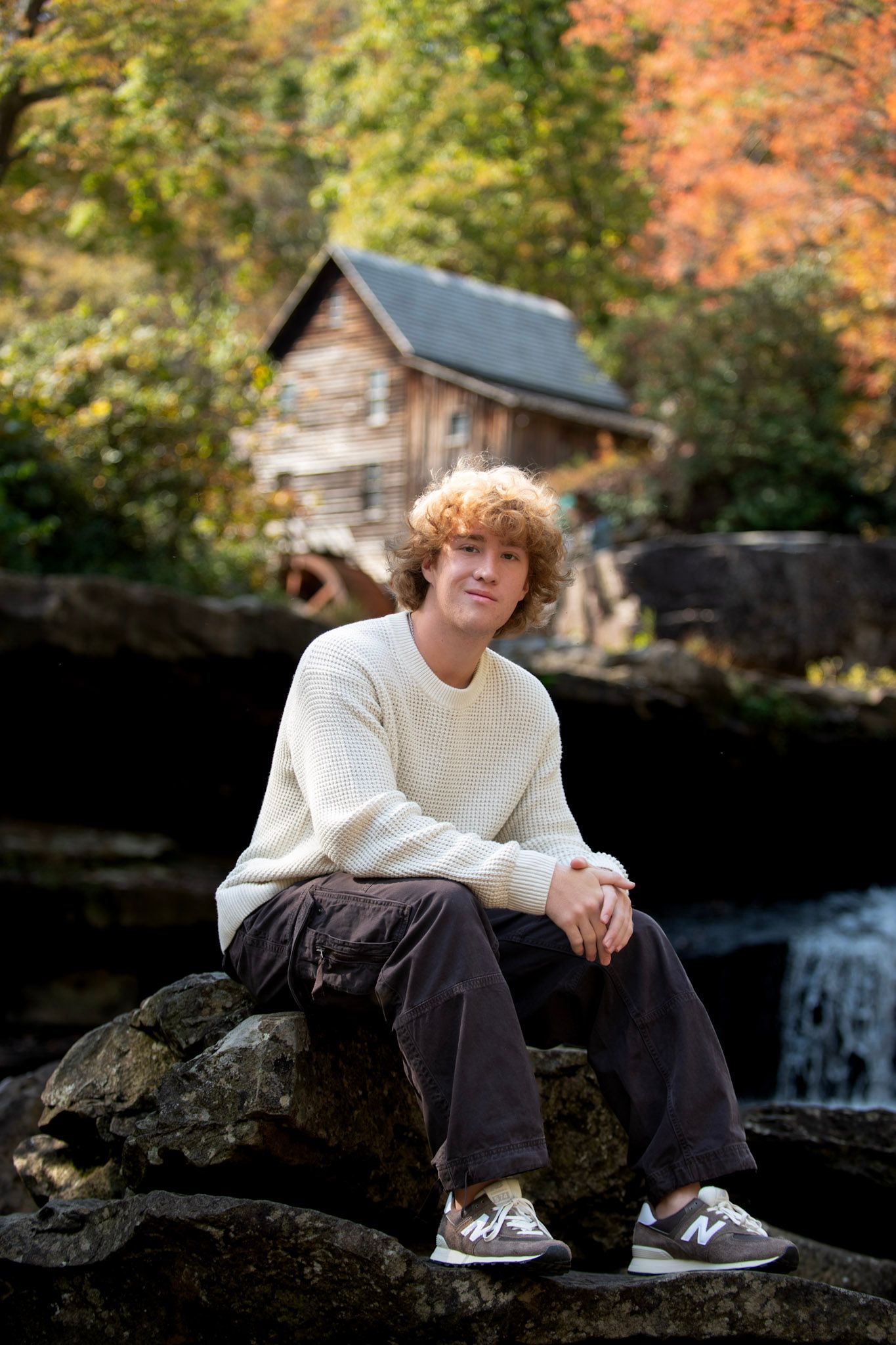 Senior portrait on rocky outcrop with autumn foliage and natural lighting.