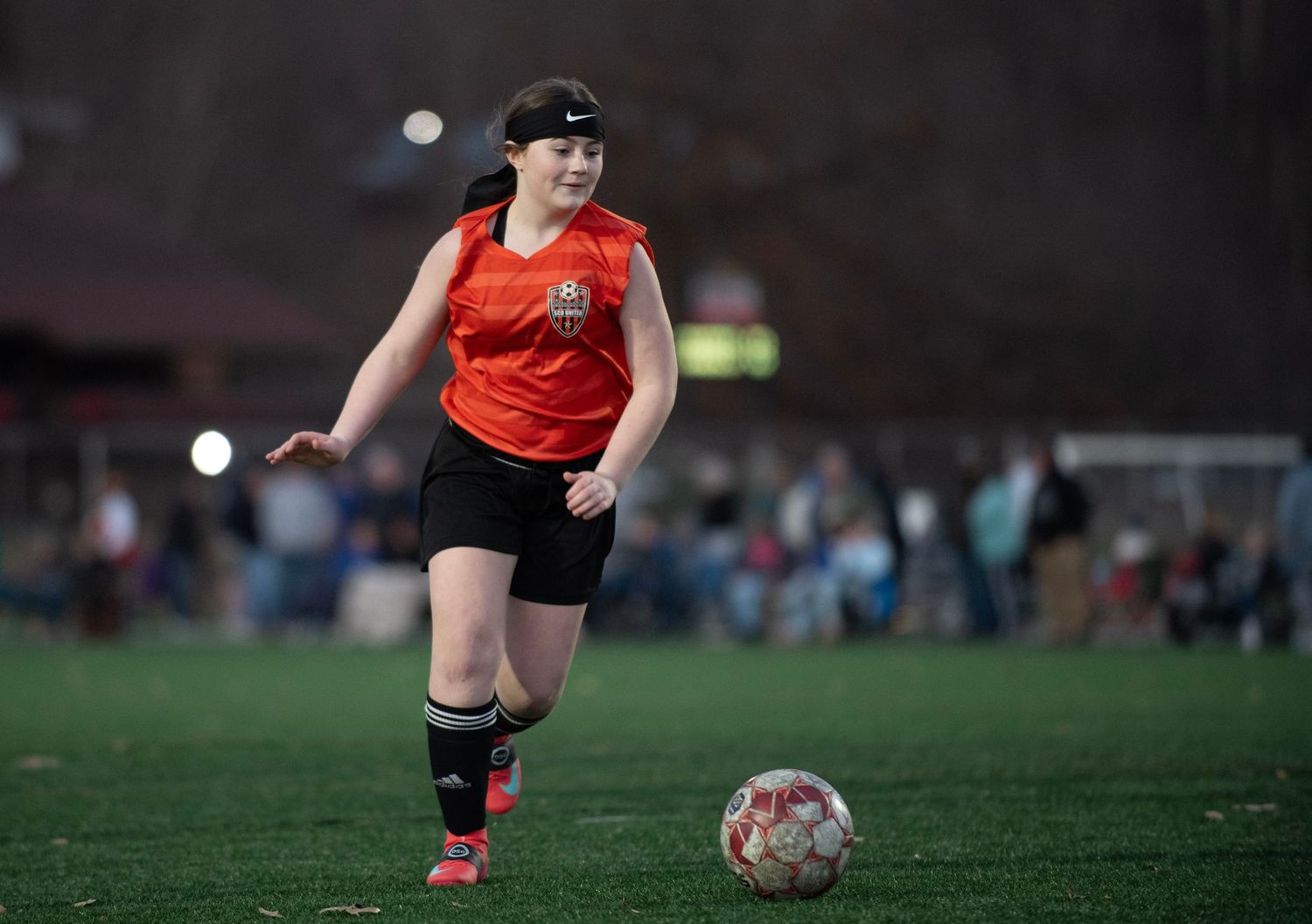 Soccer player in red jersey and black shorts dribbles ball across field during match.