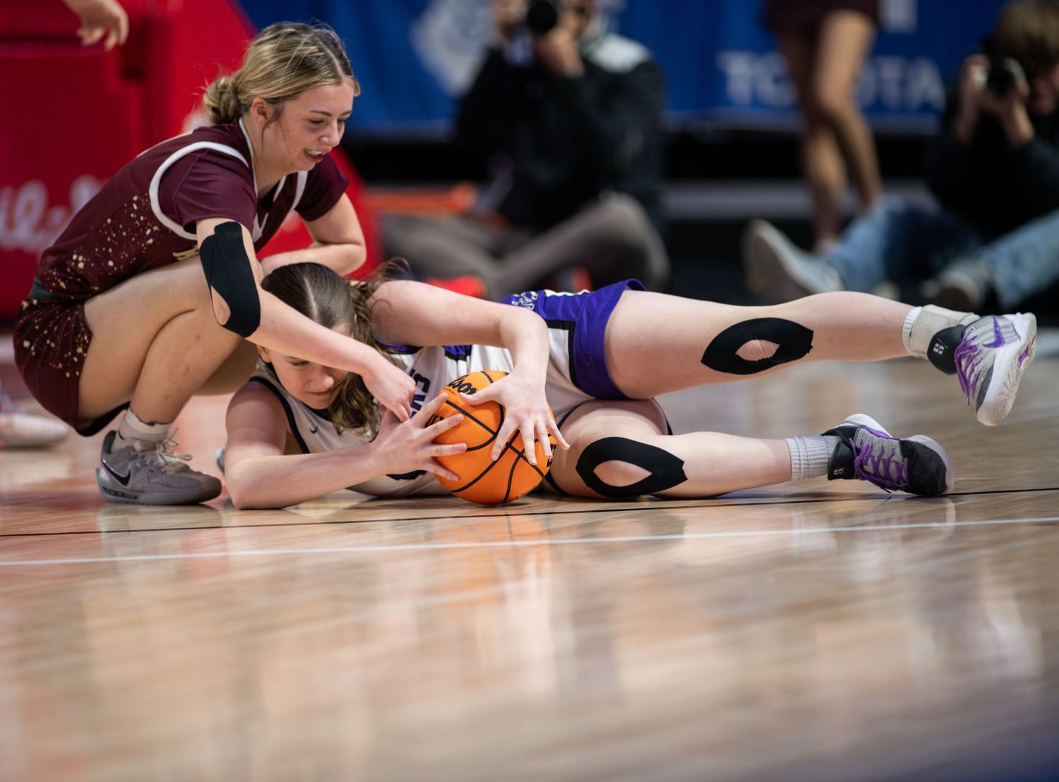 Basketball players dive and scramble for a loose ball on the hardwood court during an intense game.