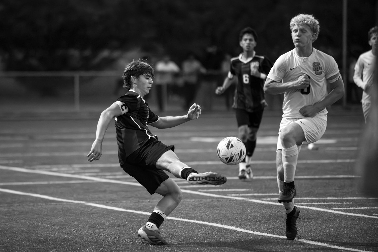 Soccer player in black uniform performs a sliding tackle against opponent in white during competitive match.