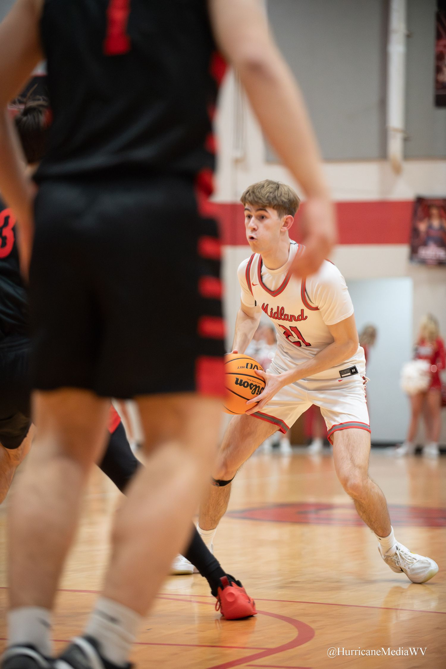 Player in white jersey crouches in defensive stance during basketball game on wooden court.