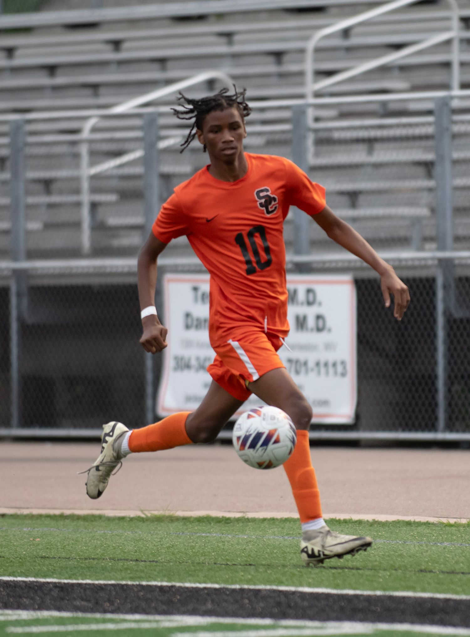 Soccer player in orange uniform performs an athletic kick on the field.