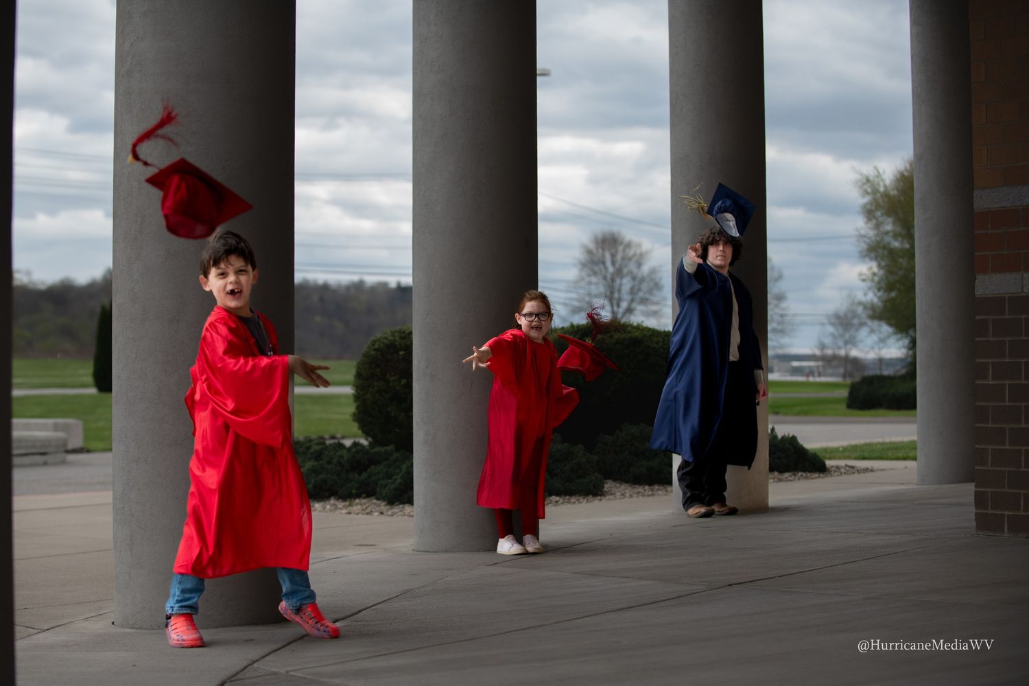 Three graduates in red and blue gowns pose dramatically between columns.