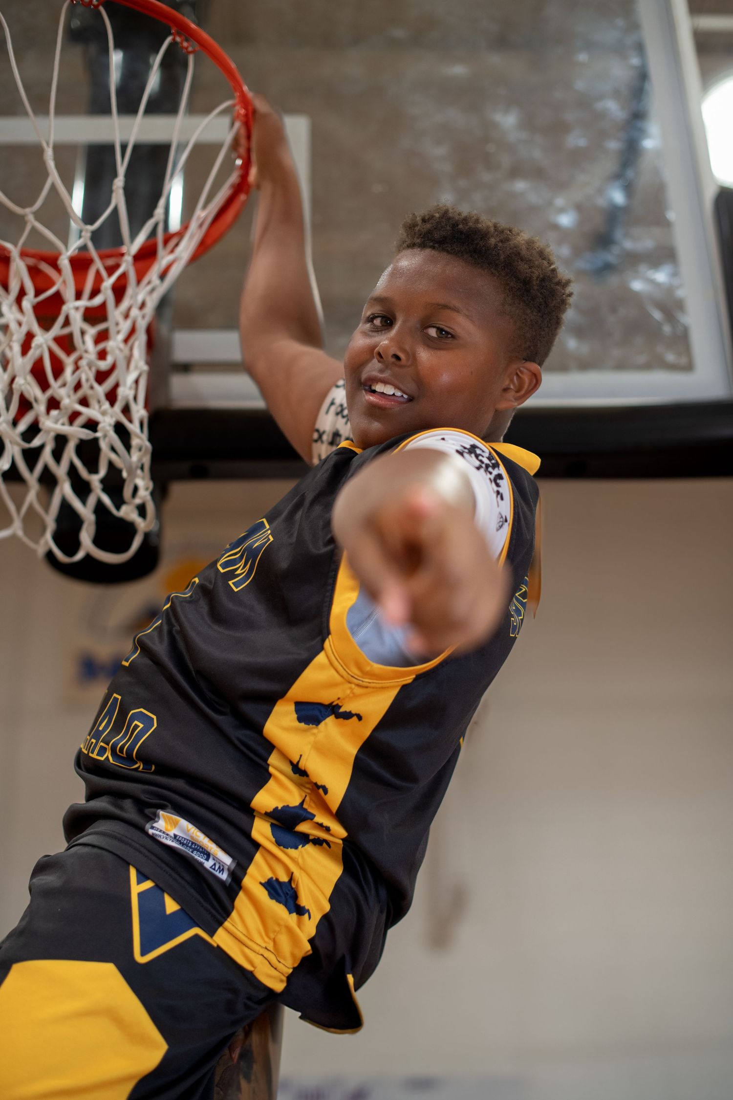 Young athlete in black and yellow jersey making a basketball layup.