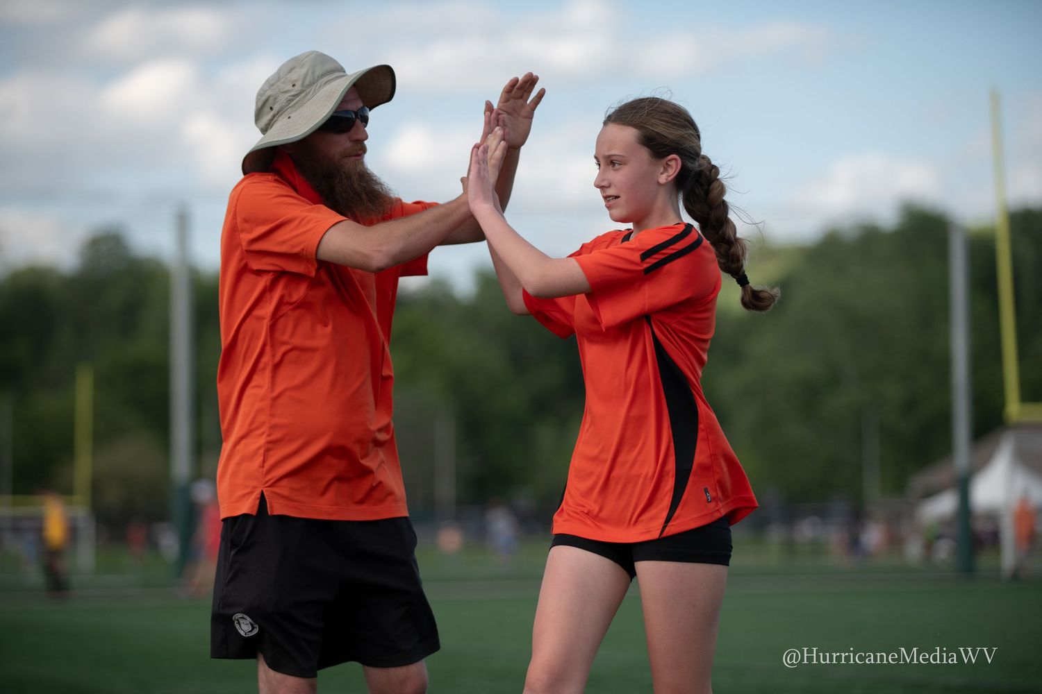 Two teammates in orange jerseys share high-five during sports game.