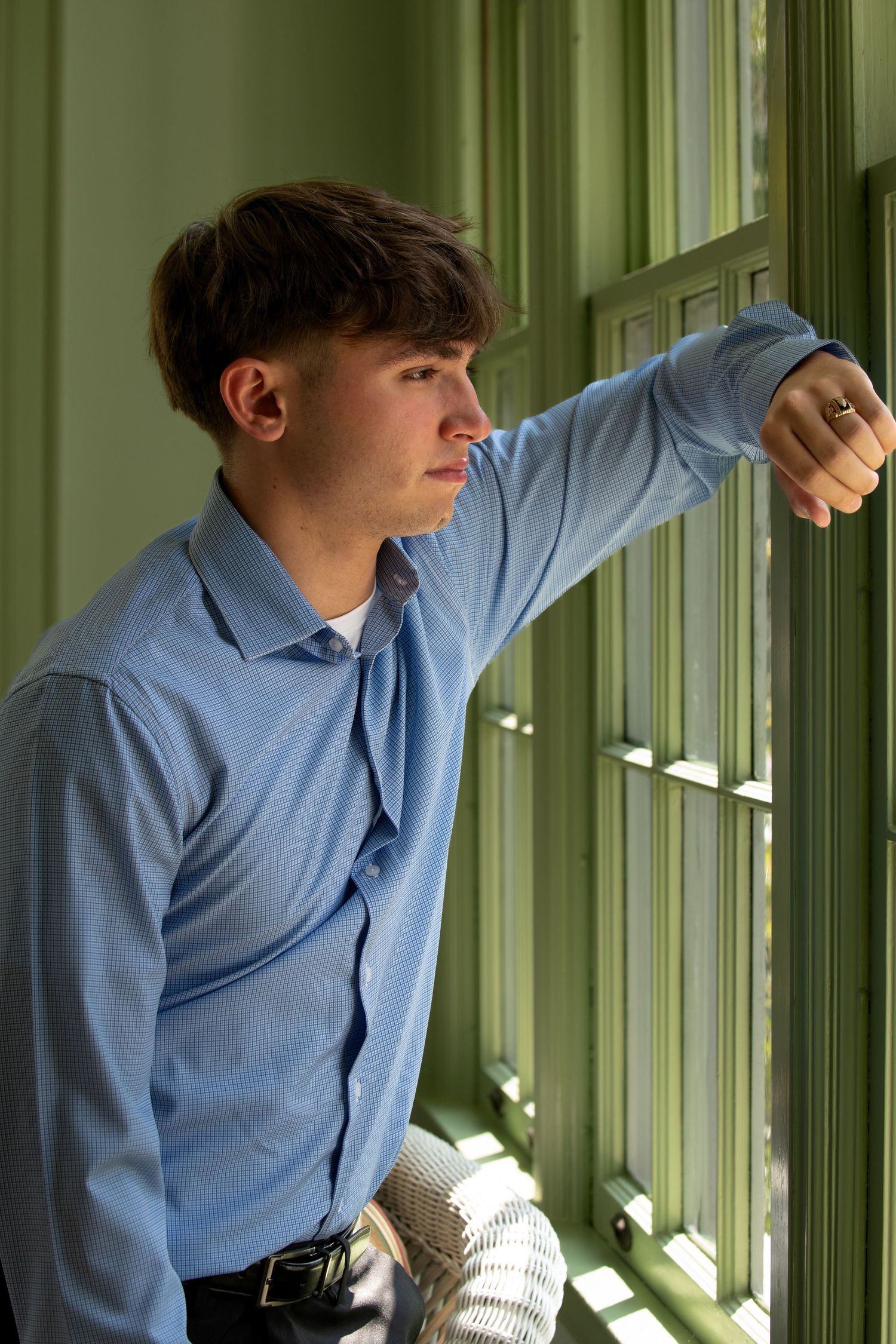 Person in light blue button-down shirt leans against window frame in green-tinted room with natural lighting.