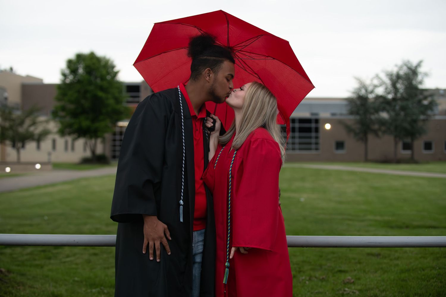 Couple shares intimate moment under red umbrella during graduation.